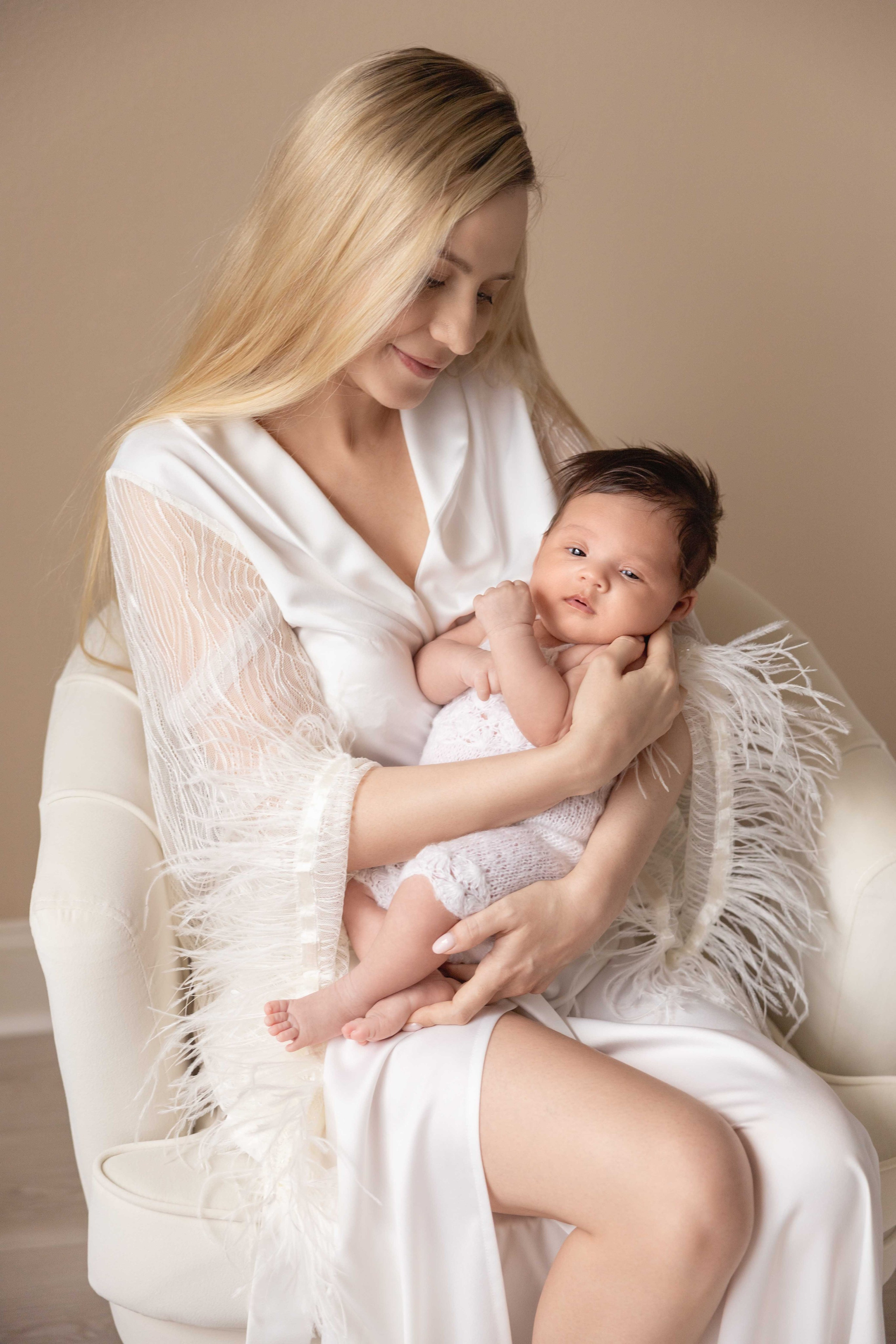 mother and newborn daughter siting in the arm chair ivory colors