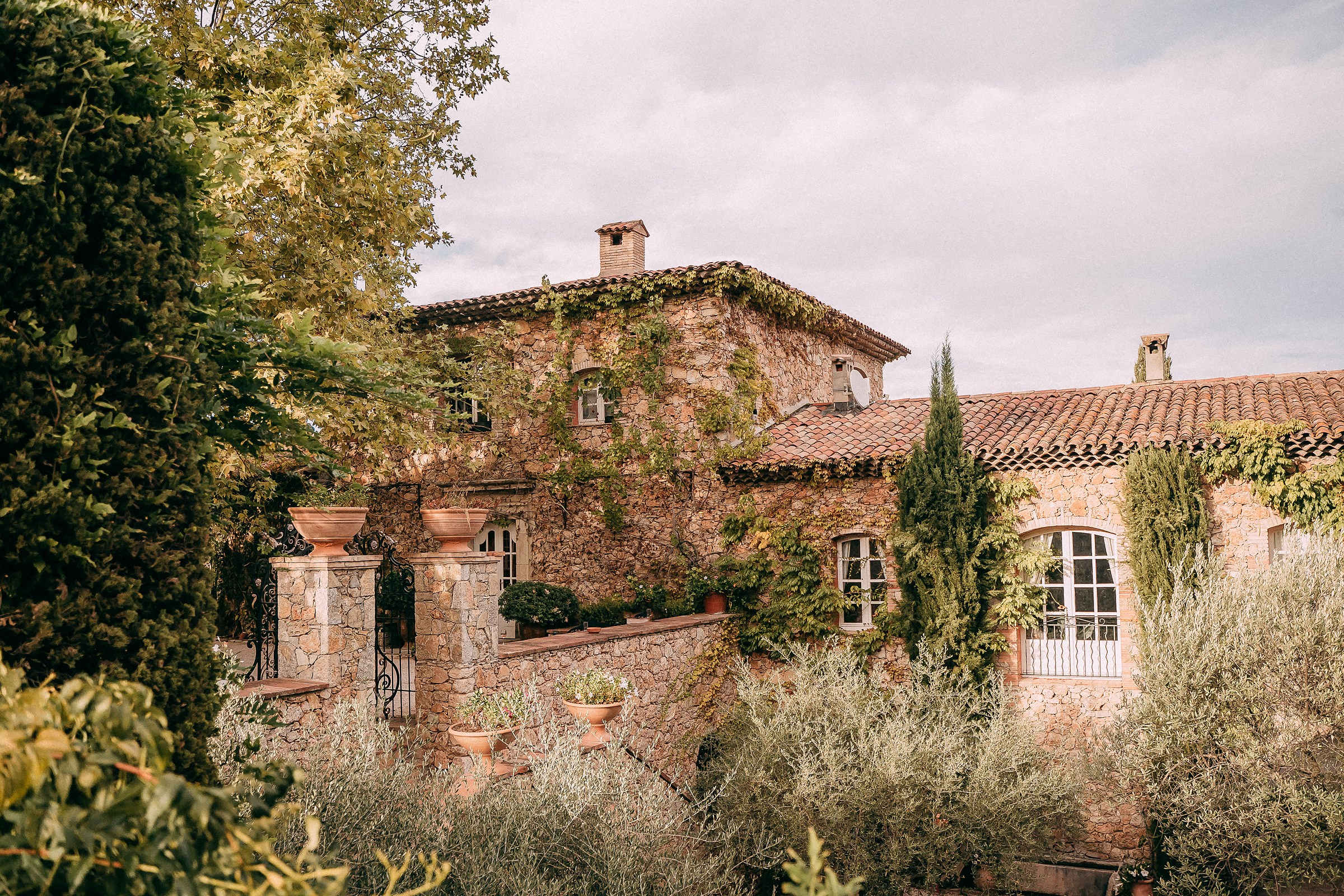 A charming view of a rustic villa surrounded by lush greenery and stone architecture under a softly lit sky.