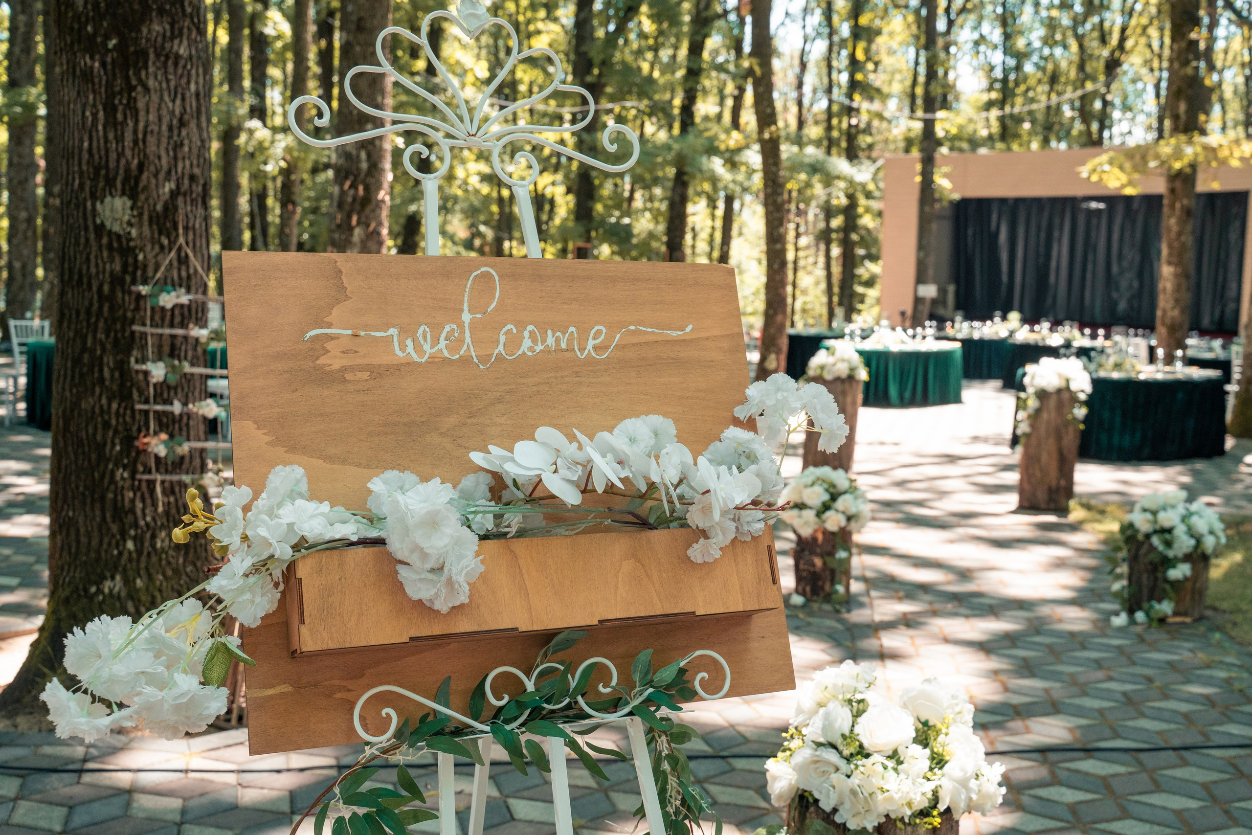 Panou de bun venit din lemn la nuntă în aer liber, decor floral alb pe șevalet, nuntă în pădure București, logistică evenimente, incadru.ro.