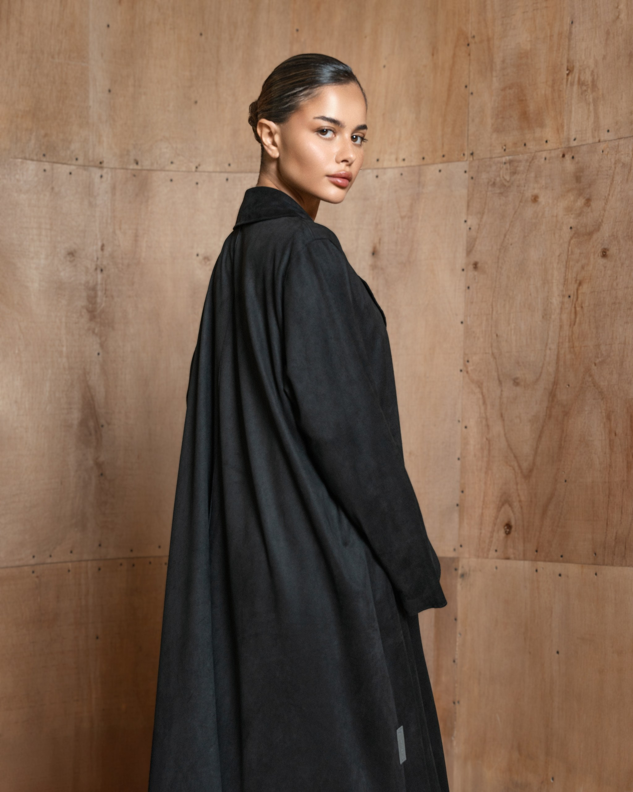 Stylish lookbook shot featuring a woman wearing a black coat by a wood-textured wall