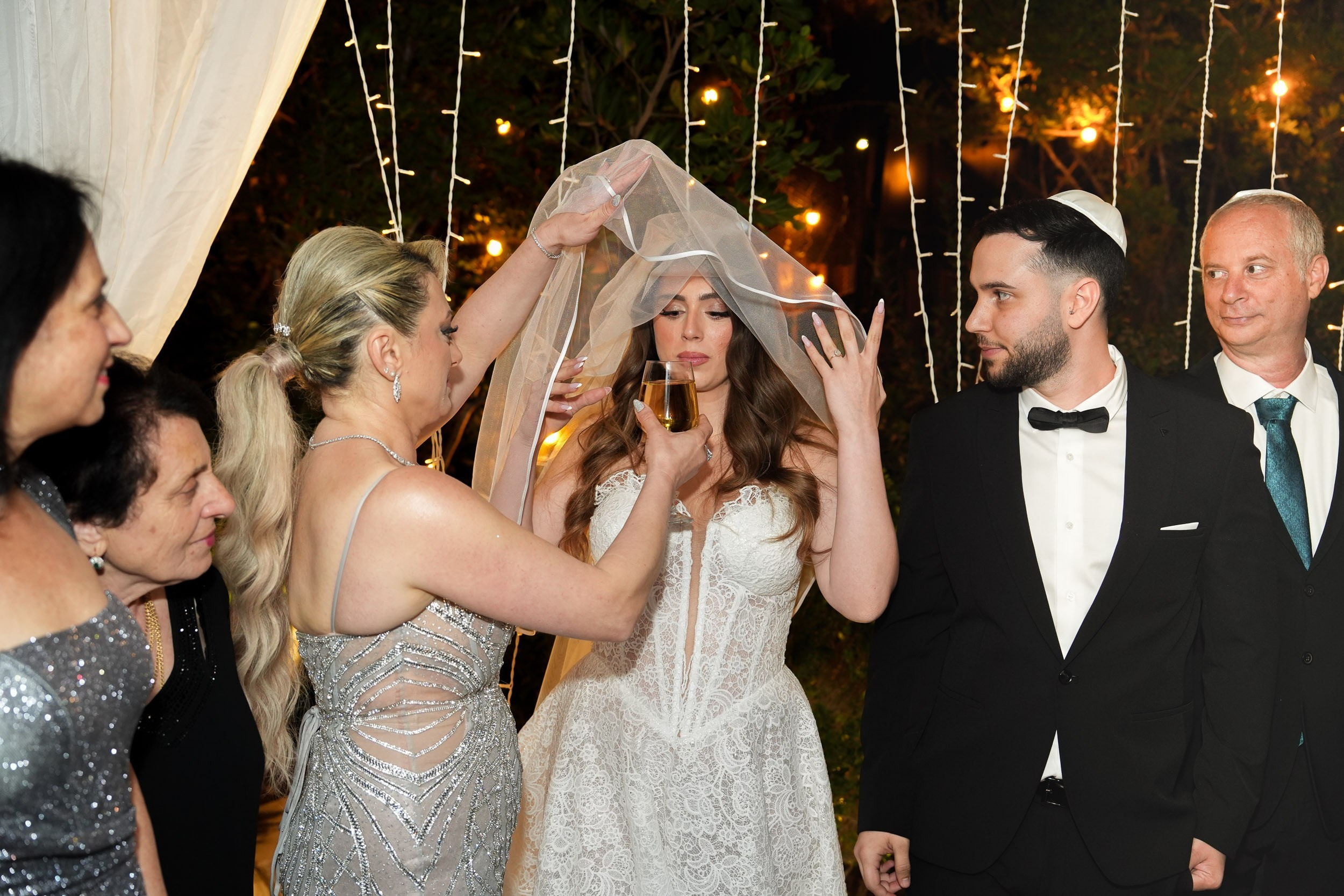 A woman adjusts the bride’s veil while the groom watches
