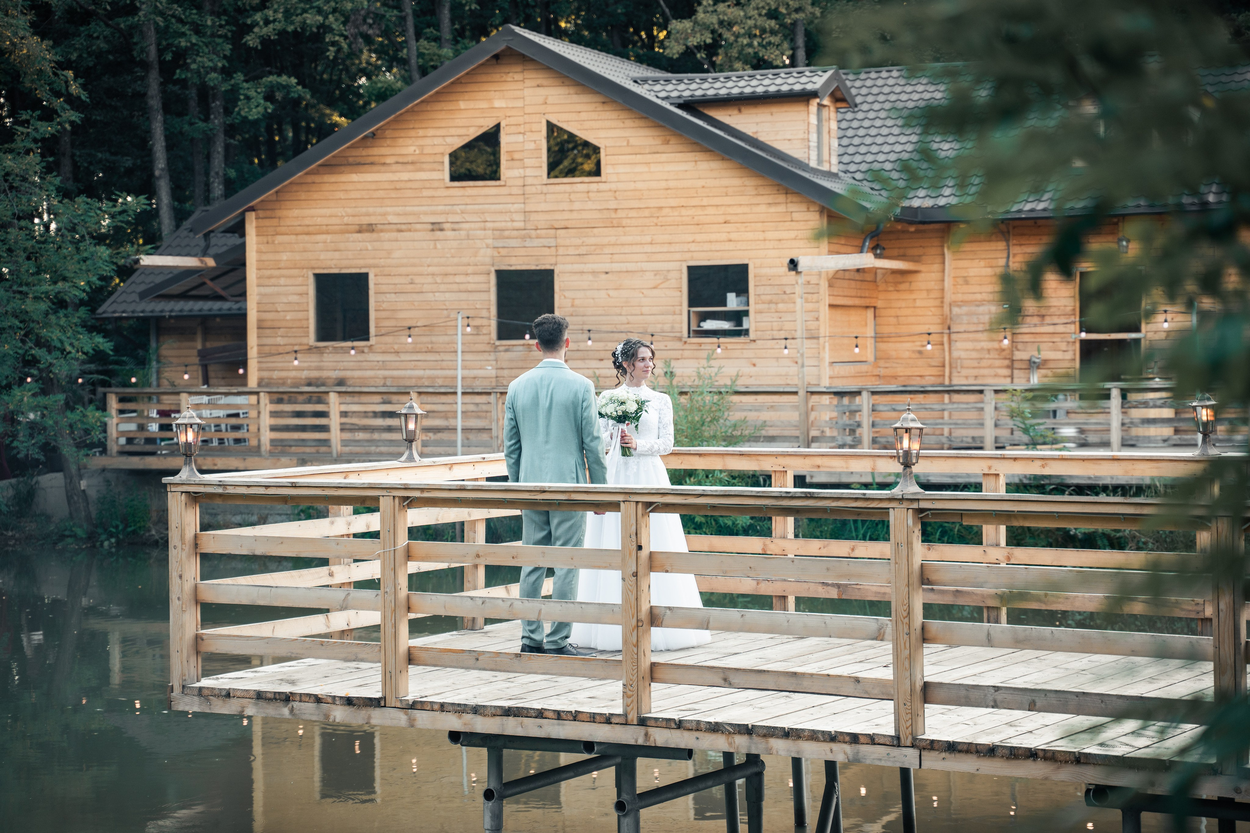 Portret miri pe un ponton de lemn în fața unei cabane rustice, reflexie în lac, nuntă la munte sau pădure, incadru.ro.