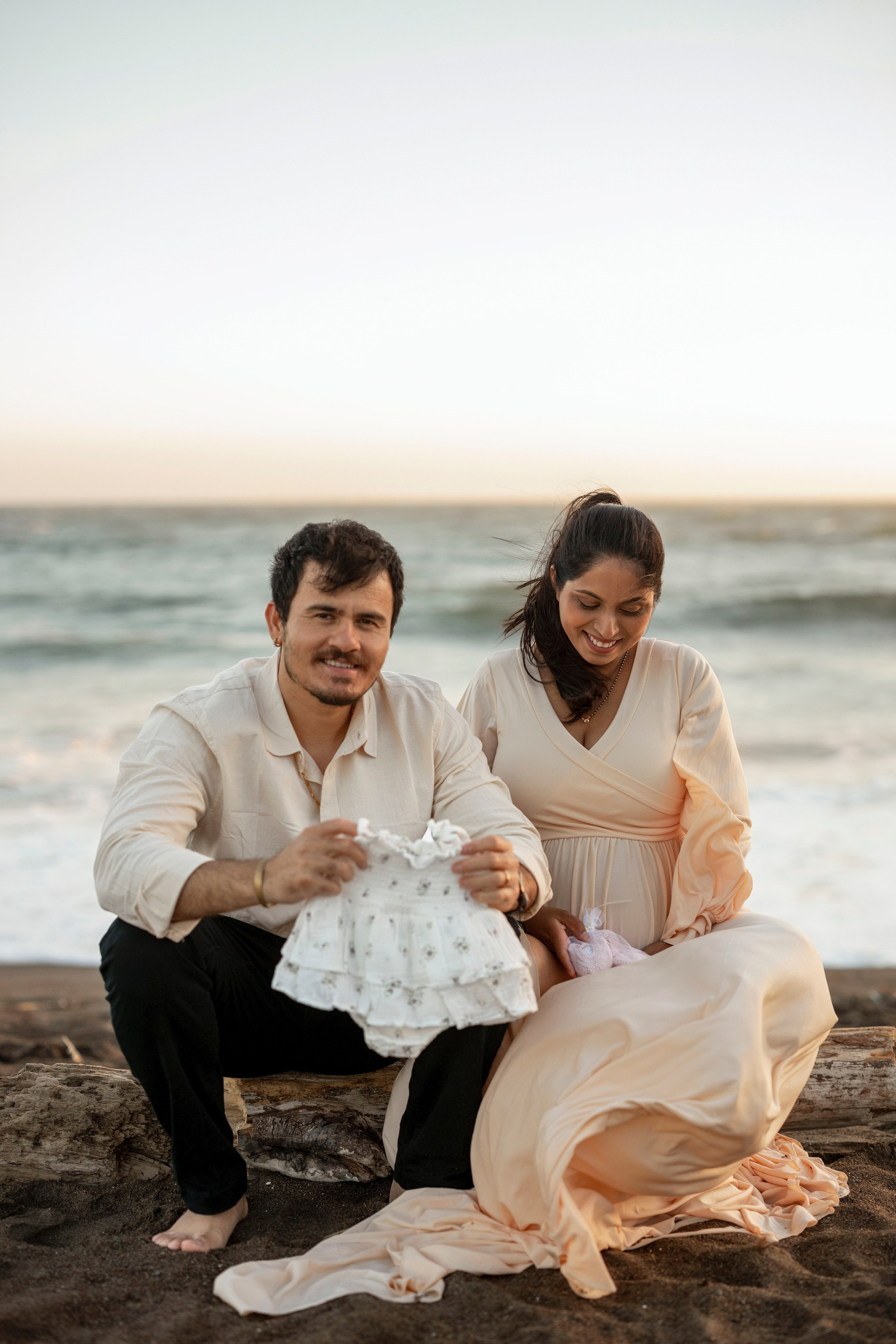 Outdoor beach maternity photography with couple cuddling by shoreline