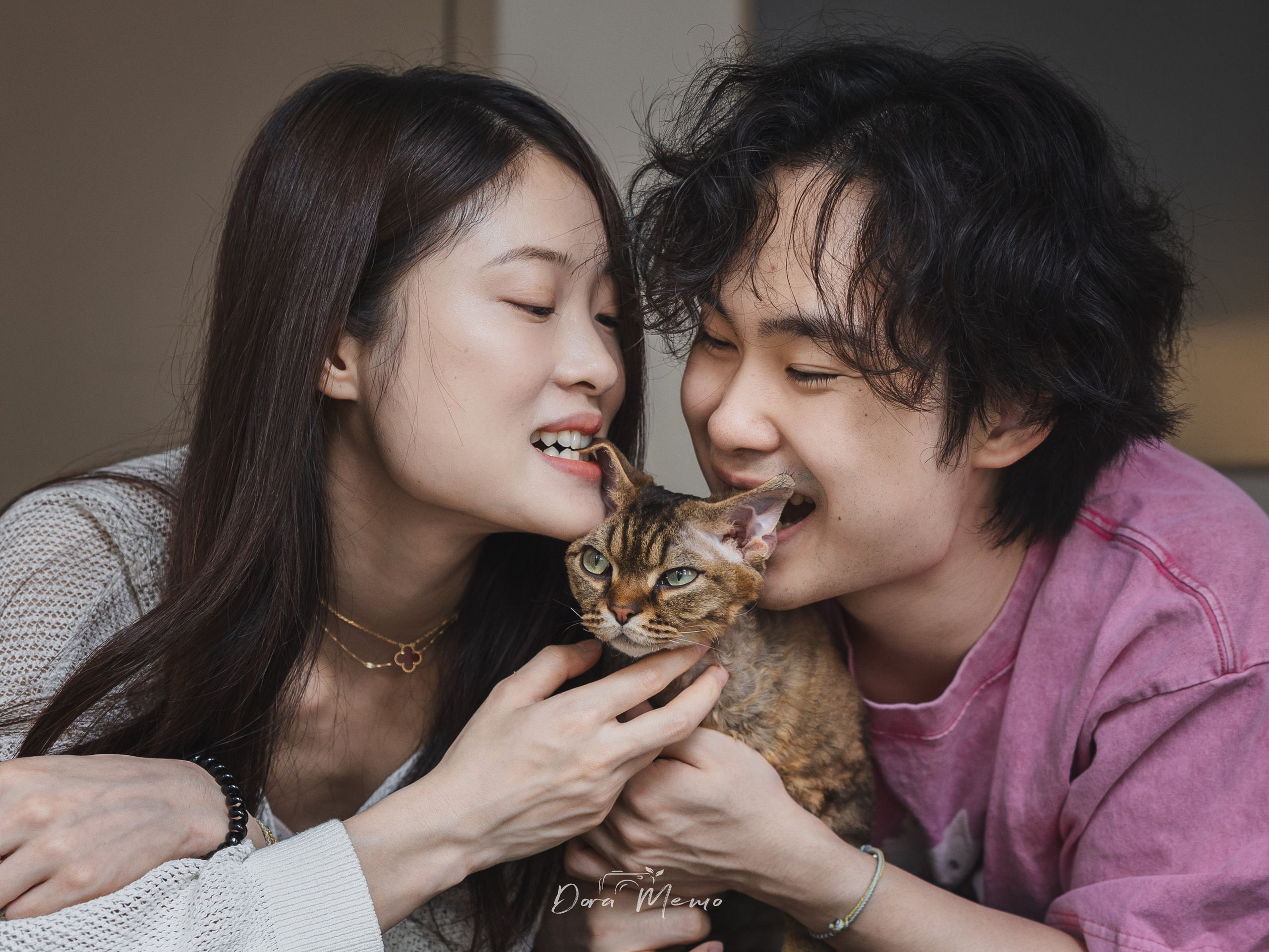 A young couple cuddles close with their cat in a warm documentary-style pet family portrait.