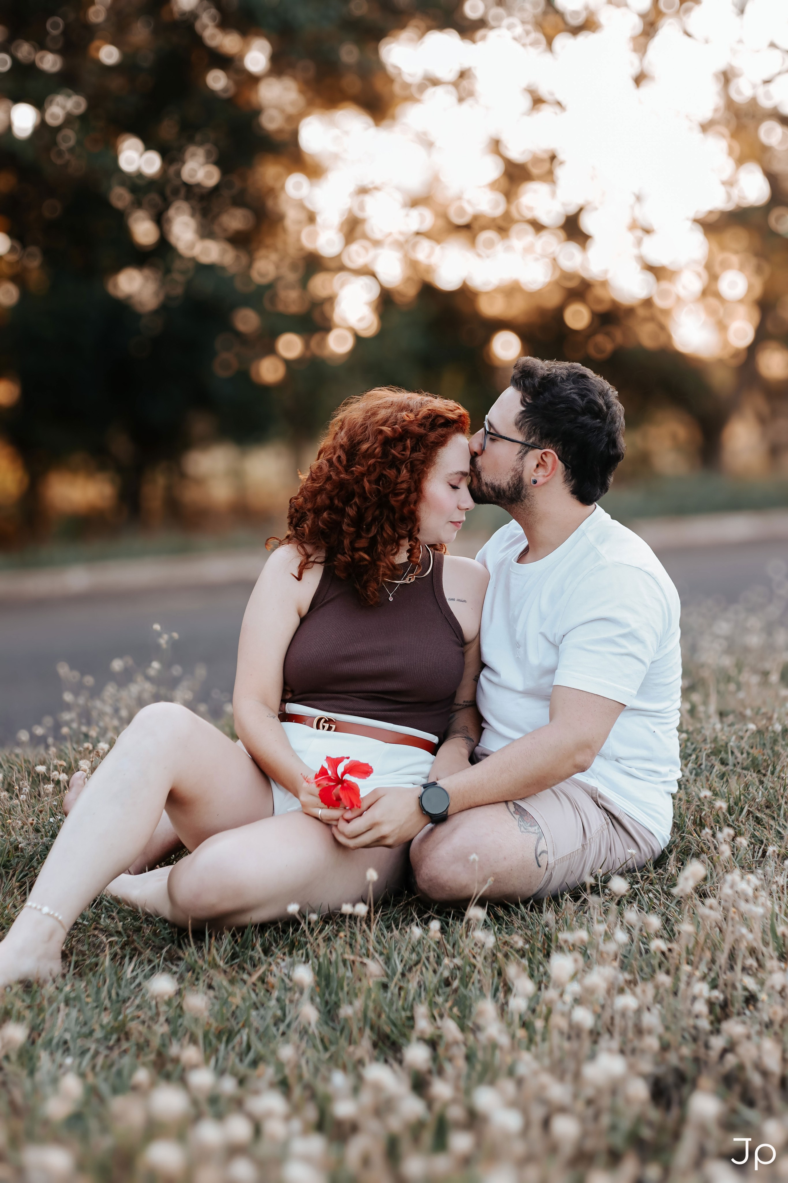 Casal sentado no chão, ela segura uma flor e se olham.
