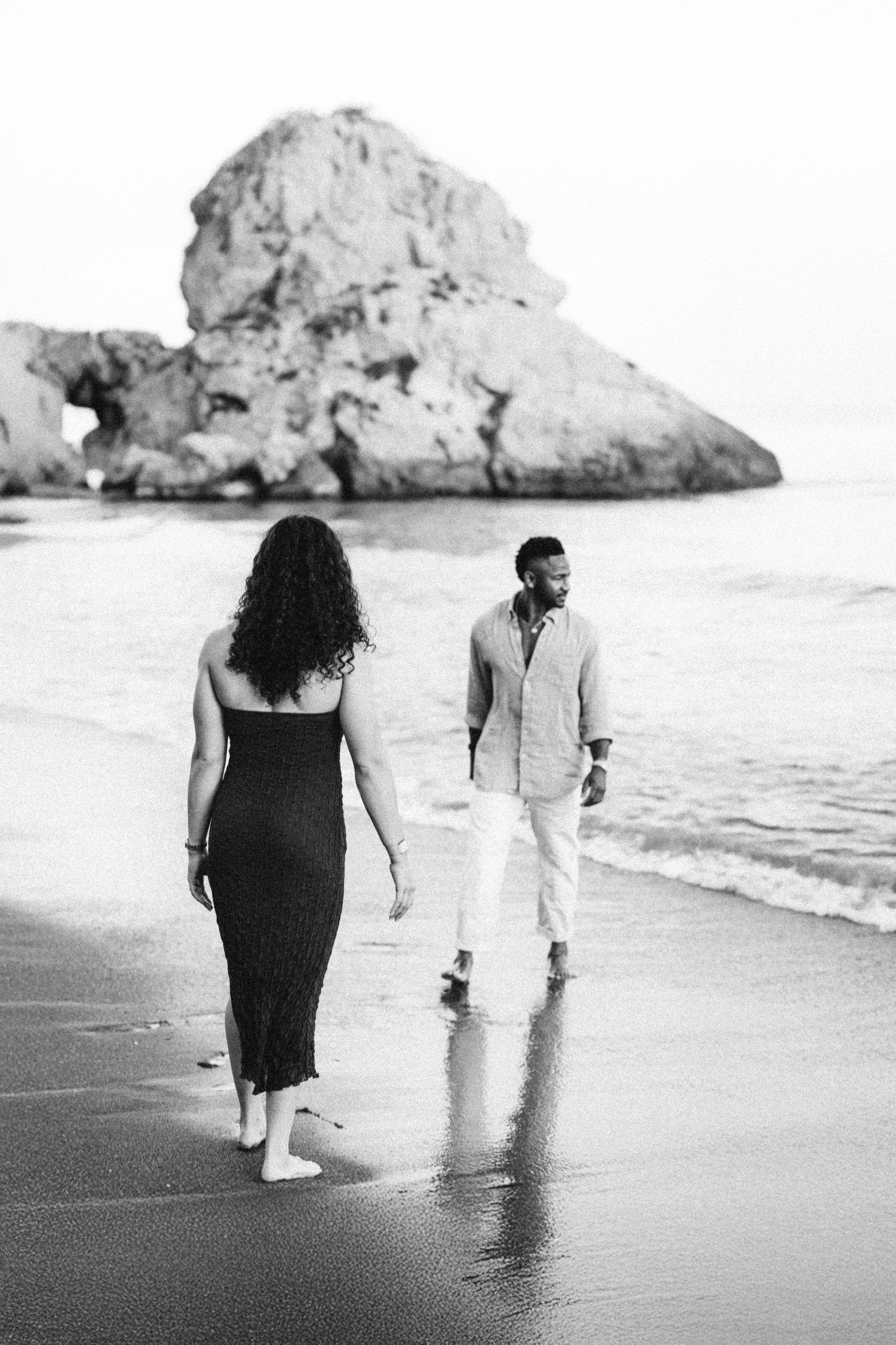 Newly engaged couple walking together along a Málaga beach following a romantic destination proposal. Coastal engagement photography in southern Spain blending dramatic rock formations and natural storytelling.