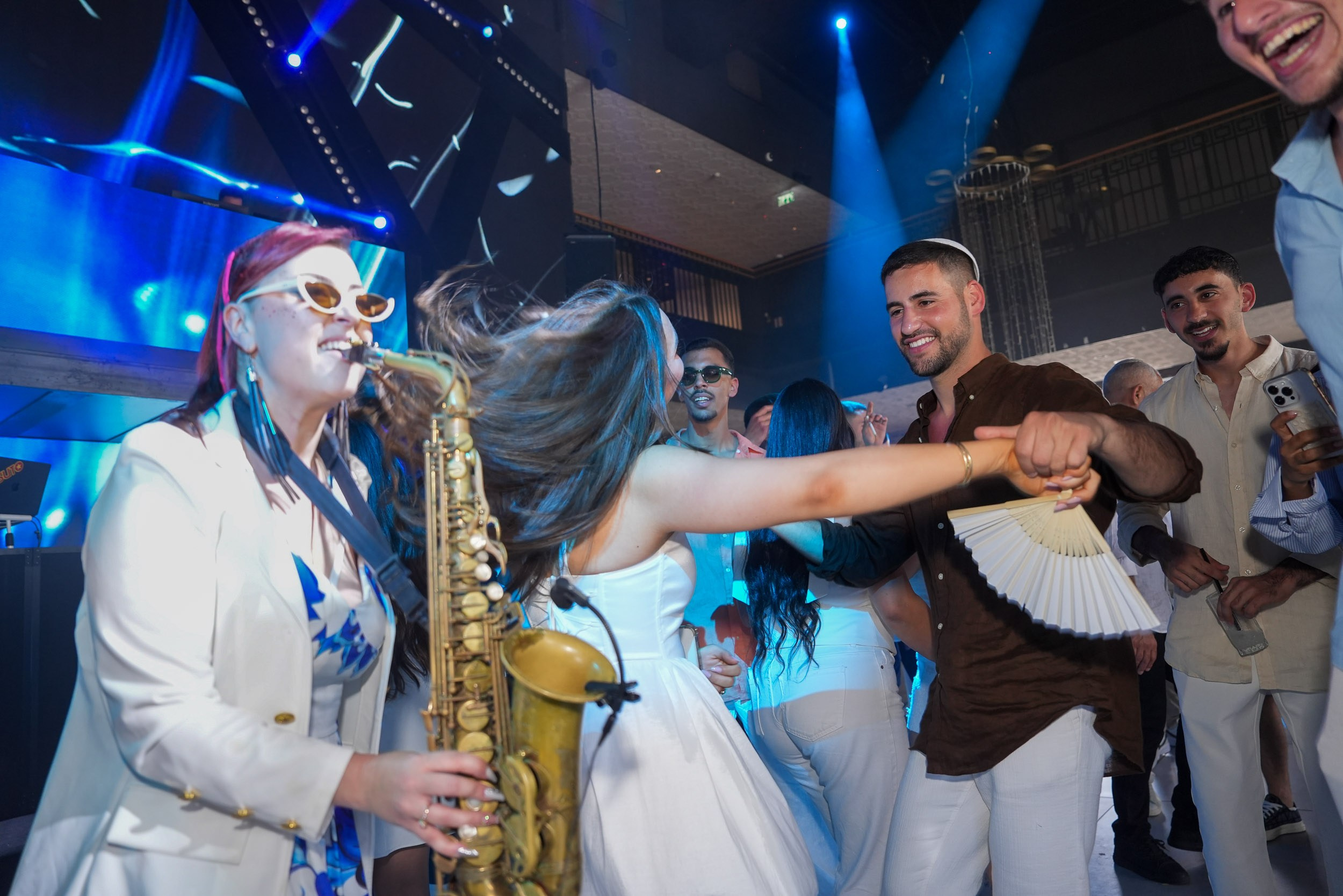 Guests dancing next to a live saxophone player during their wedding party Shani & David at Artista Event Garden in Hadera, Israel