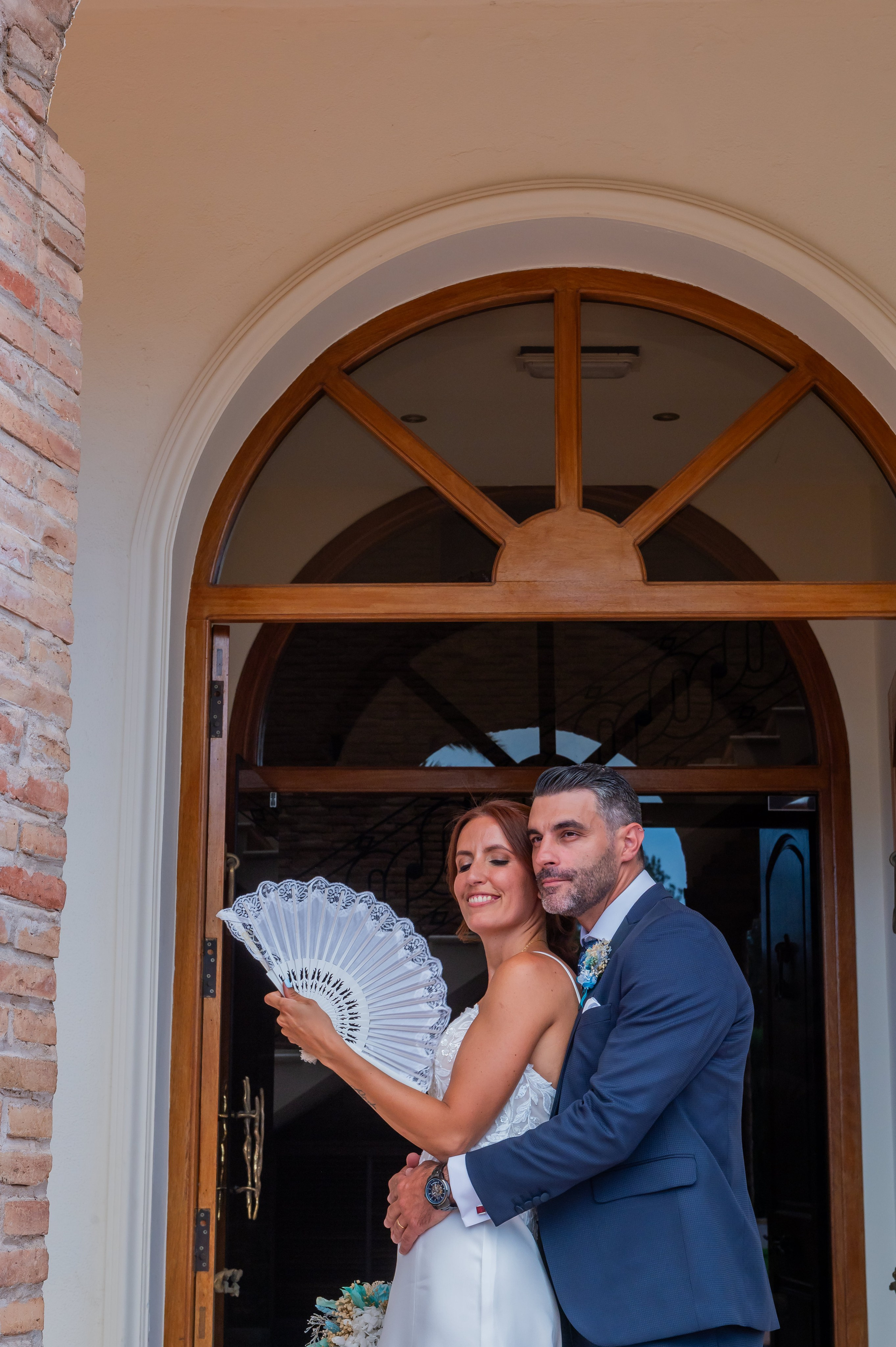 Novios con abanico bajo un arco blanco