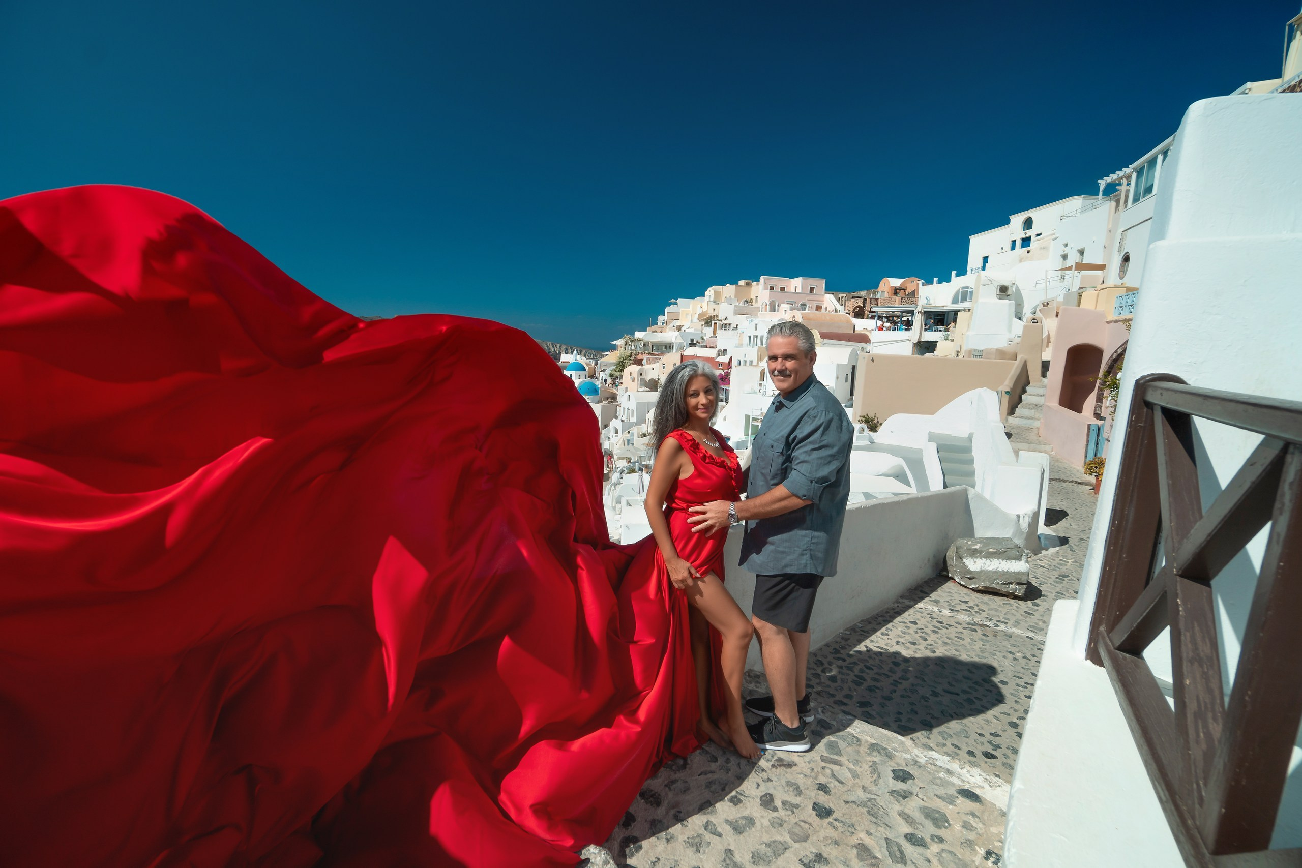 Curvy woman in red plus size flying dress with ruffles, posing against Santorini’s blue-domed cliffs.
