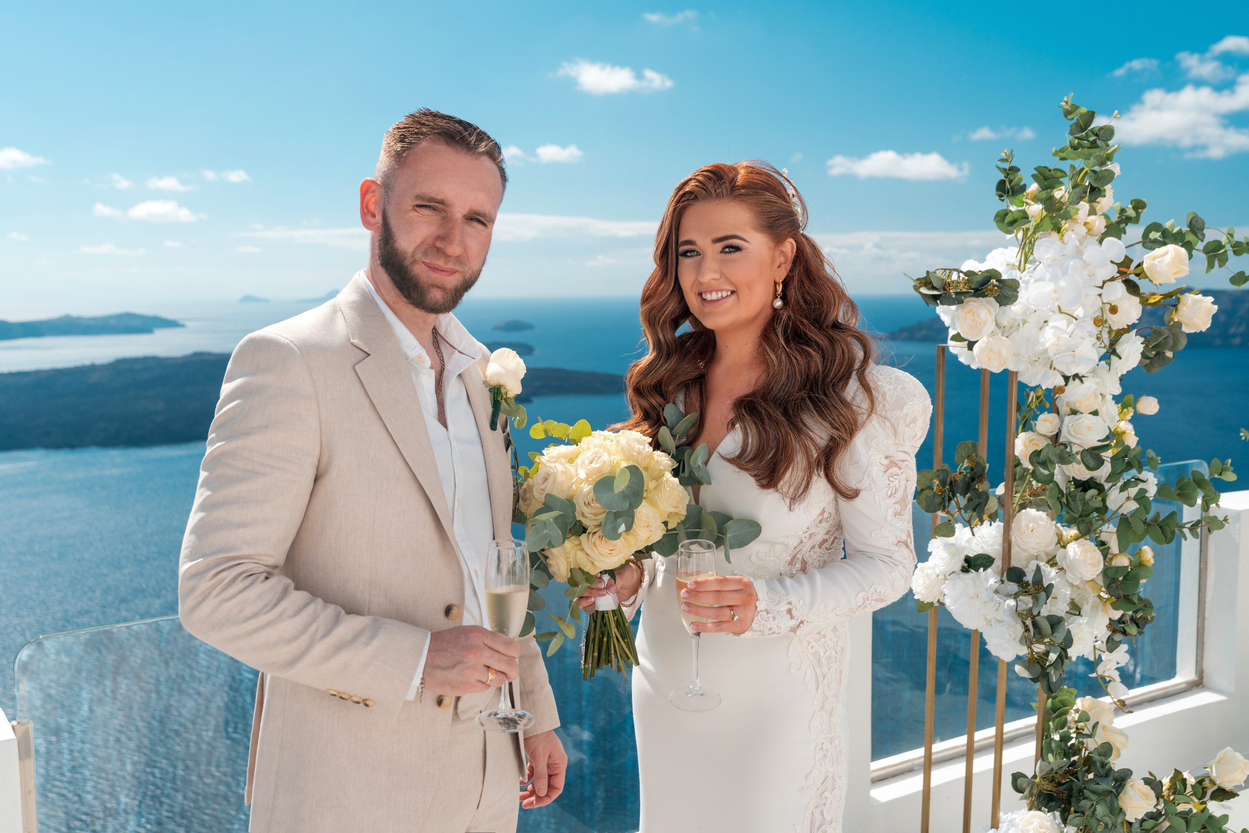 Emotional wedding couple session in Imerovigli cliffs – flying dress in soft pastel tones flowing dramatically, Santorini caldera and volcano in background