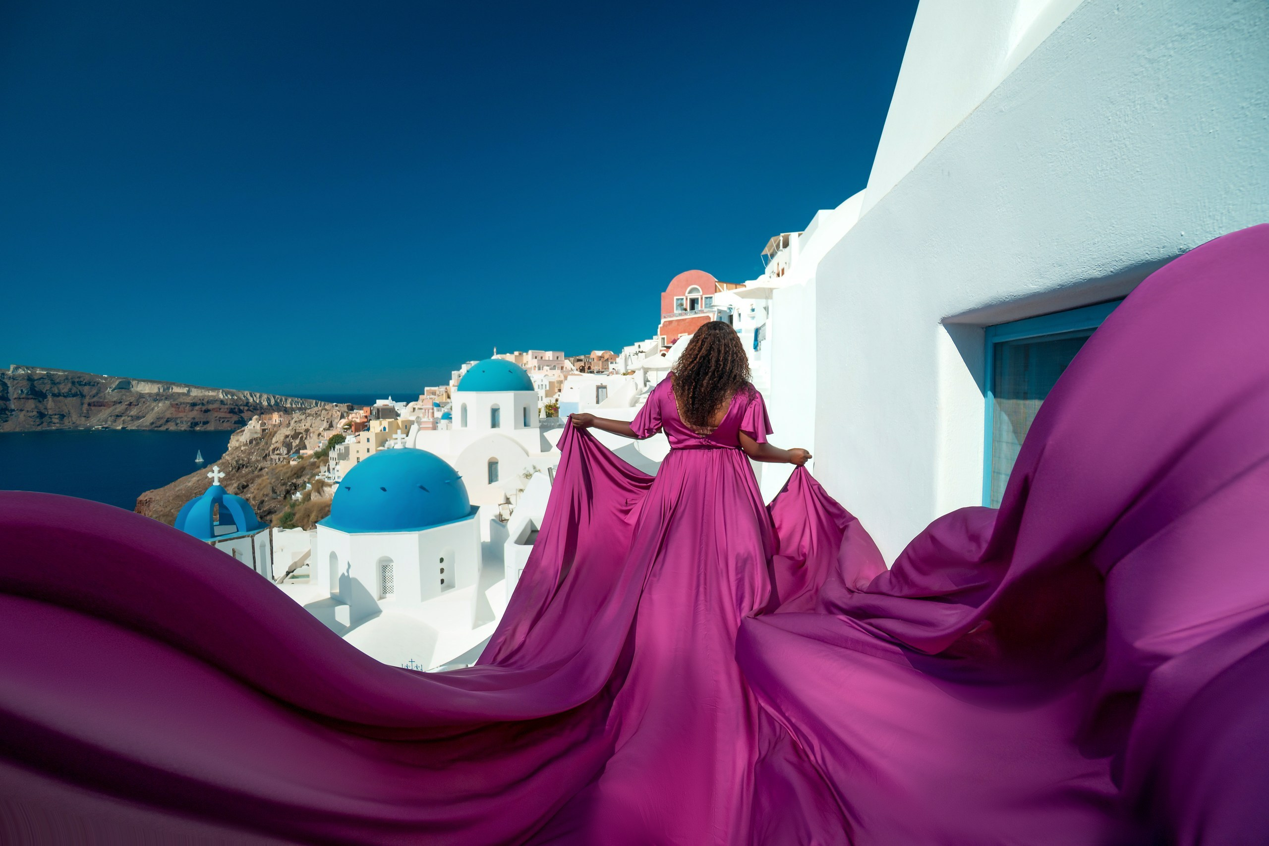 Curvy model in purple plus size flying dress L-XXXL, twirling against Santorini's white-washed cliffs and sea.