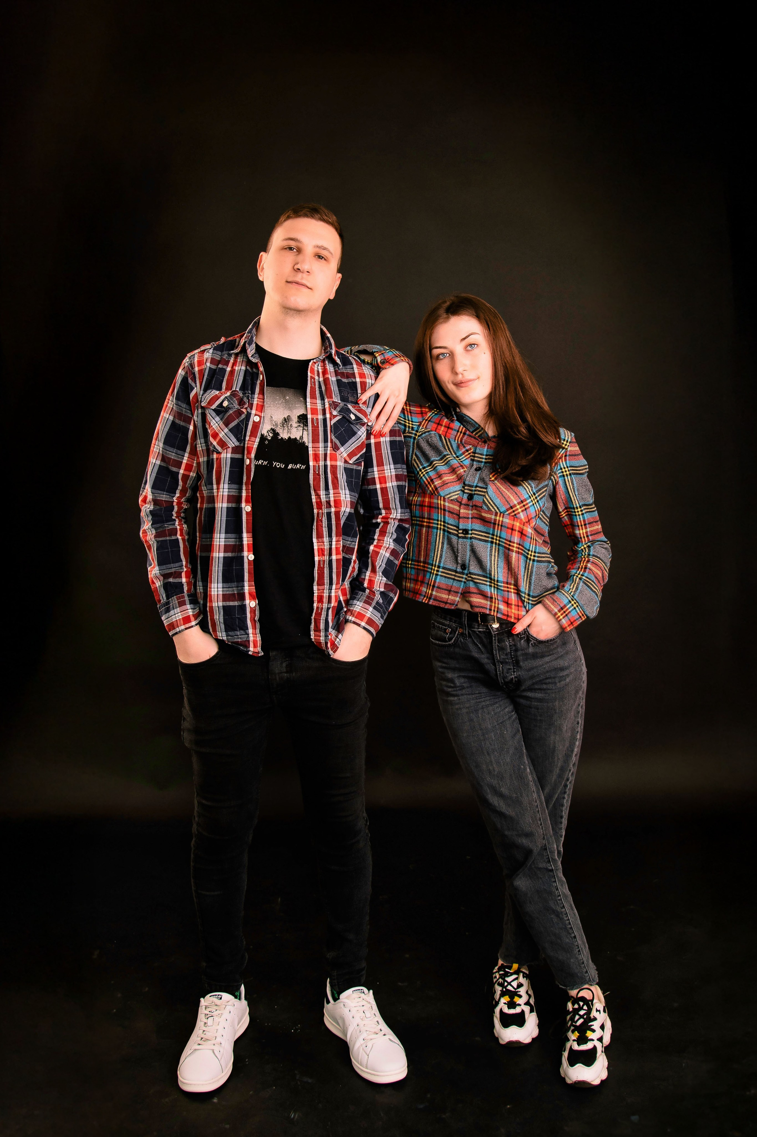 Zwei Personen stehen im Studio vor dunklem Hintergrund, professionelles Ganzkörper-Porträt.