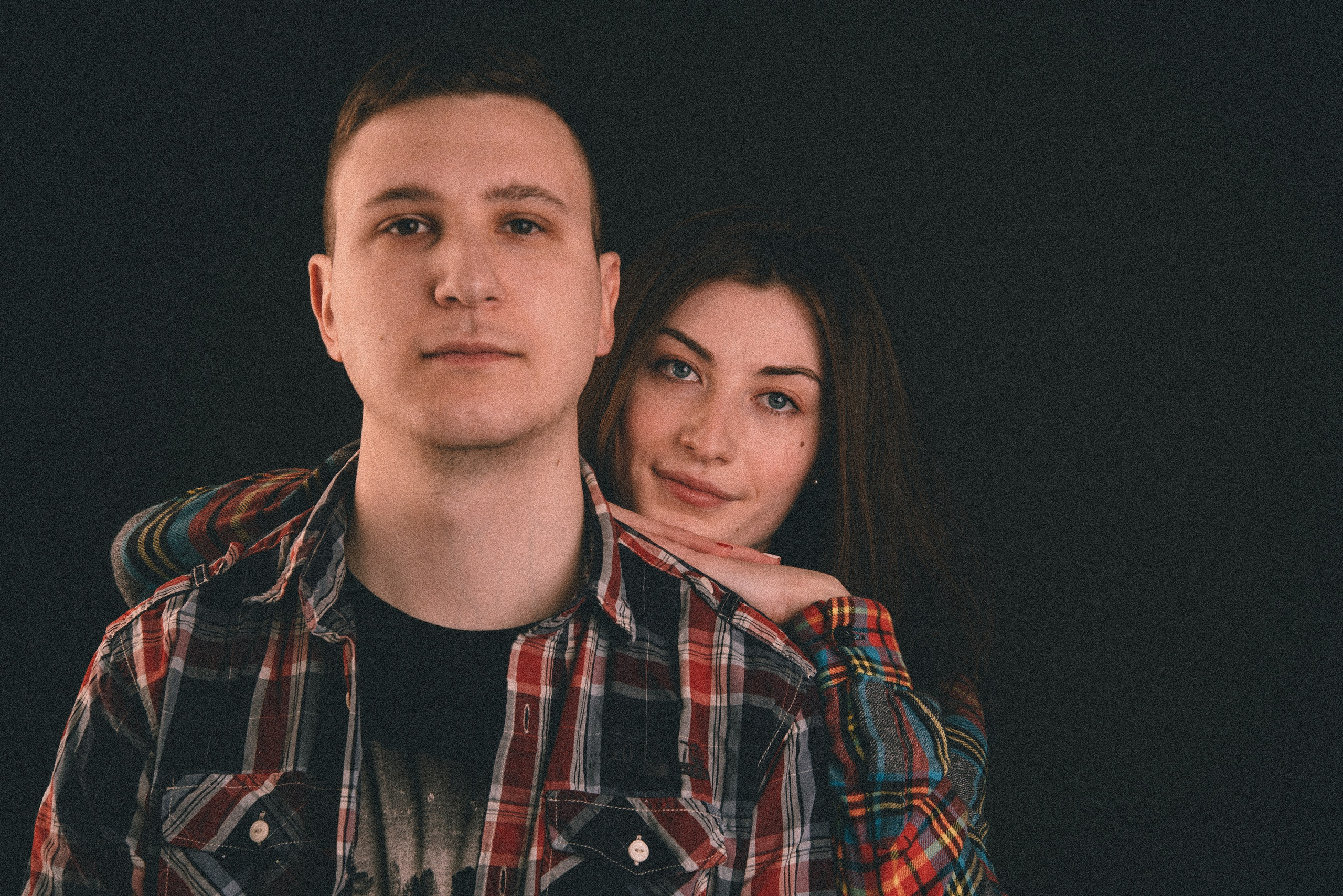 Zwei Personen posieren gemeinsam vor dunklem Hintergrund, modernes und schlichtes Porträt.