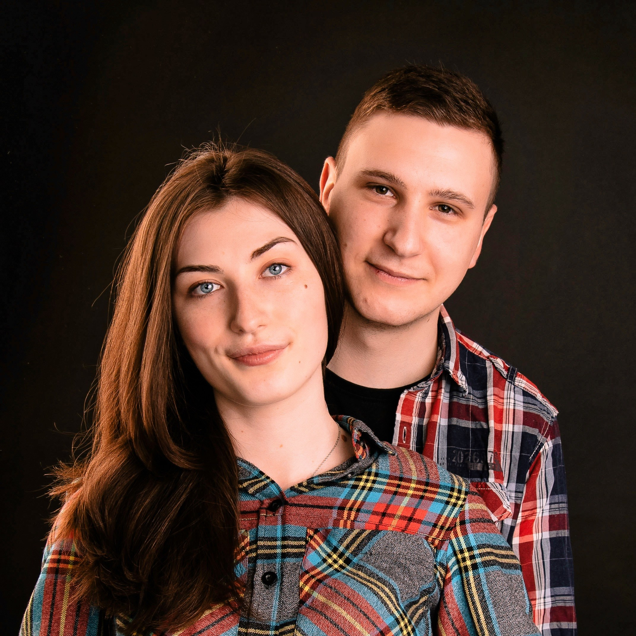 Eine Person sitzt, die andere steht dahinter und legt eine Hand auf die Schulter, klassisches Studio-Porträt.