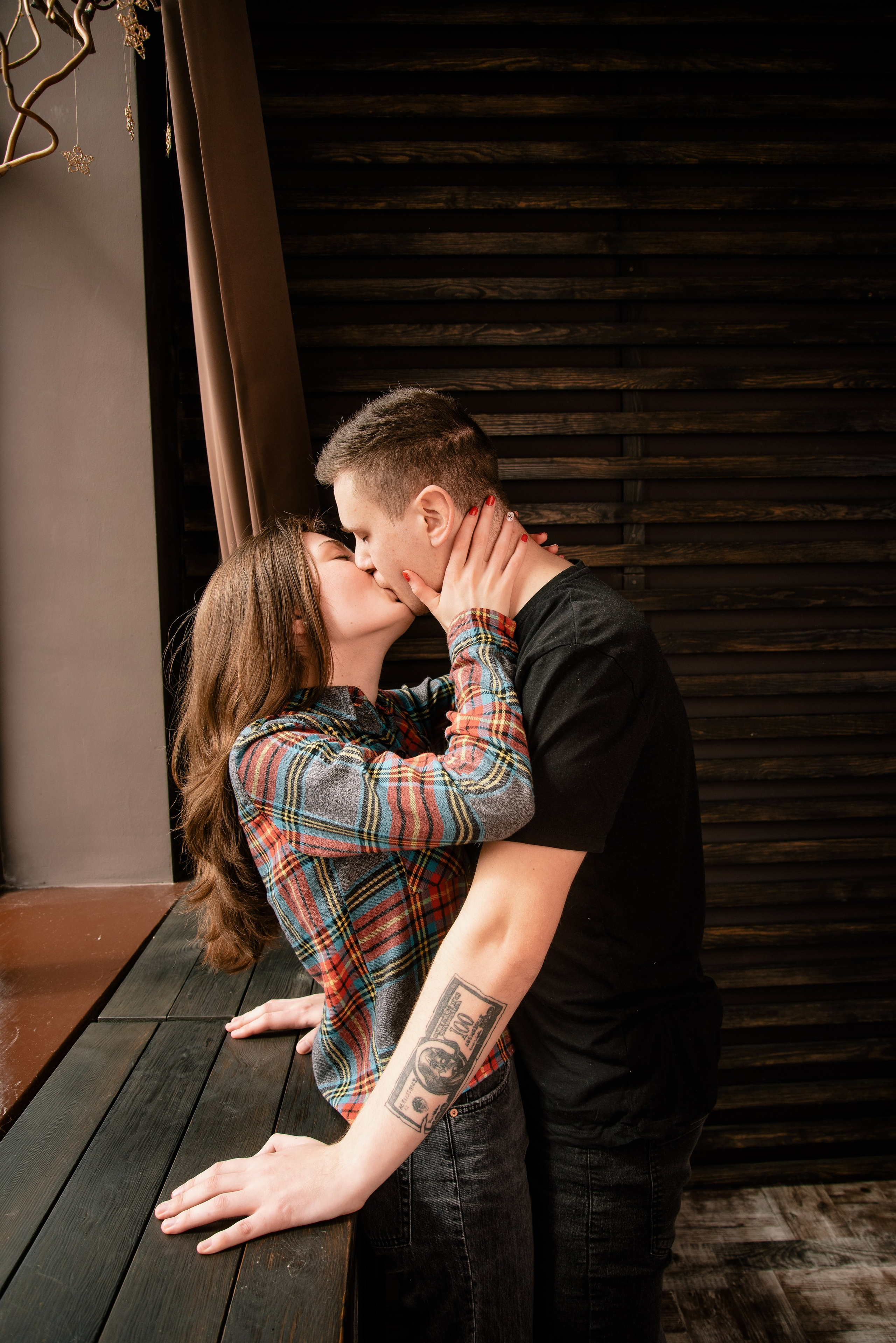 Eine Person sitzt auf dem Fensterbrett, die andere steht davor, warmes Licht und modernes Paarporträt.