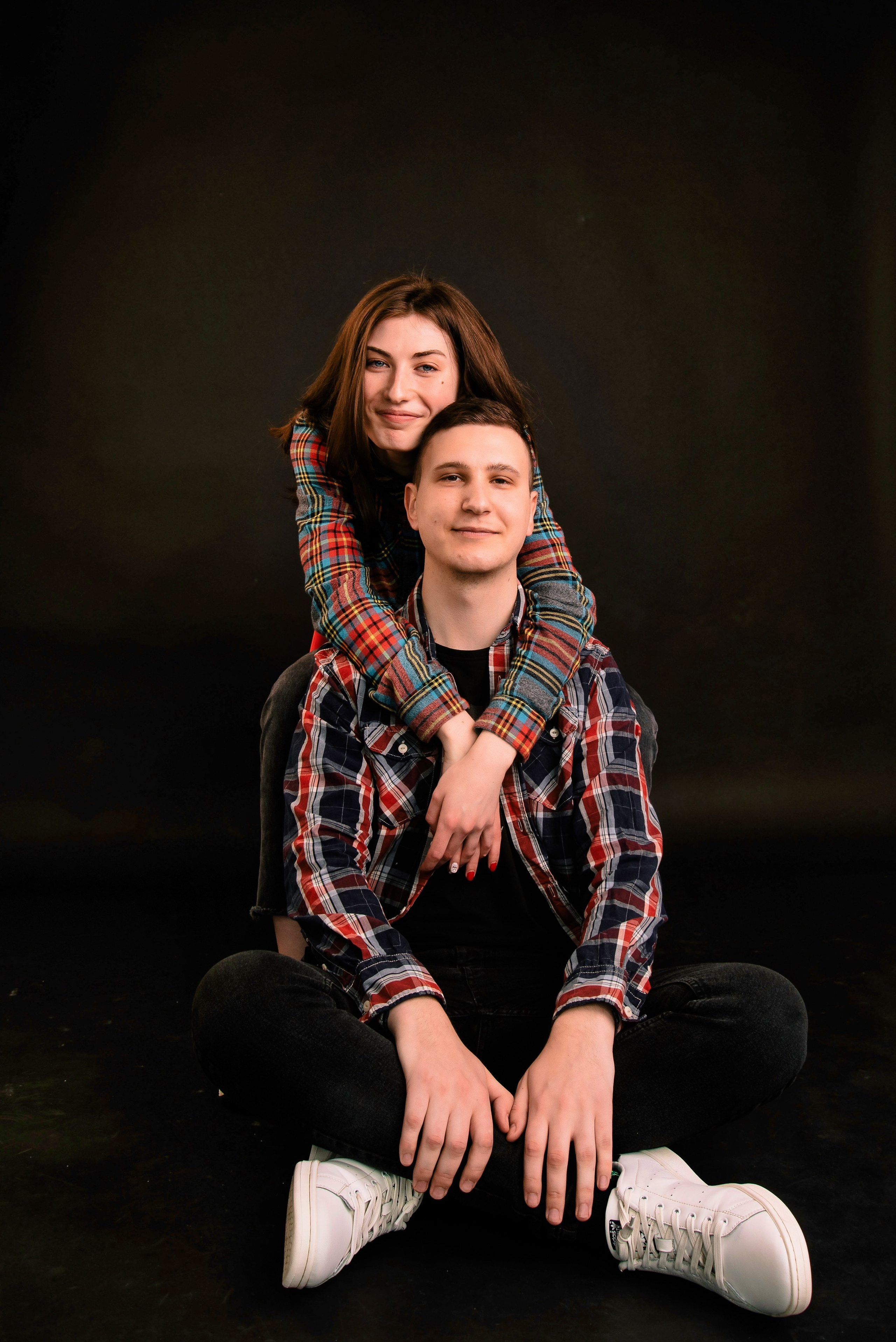 Ein Paar sitzt zusammen vor dunklem Hintergrund, ruhiges und modernes Porträtfoto.