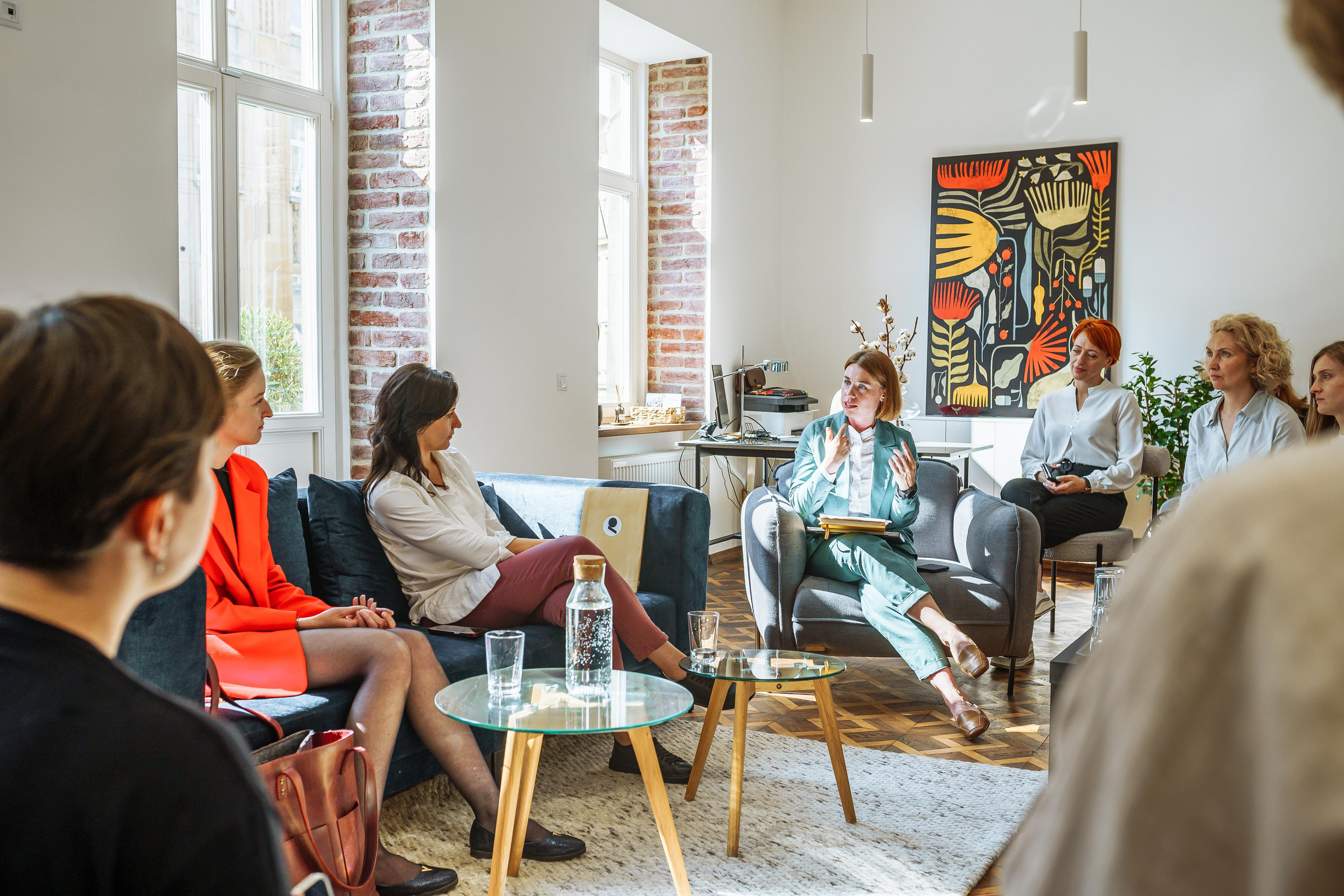 Розмова працівників в офісі компанії, по центру зали стоять маленькі столи, а працівники сидять довкола