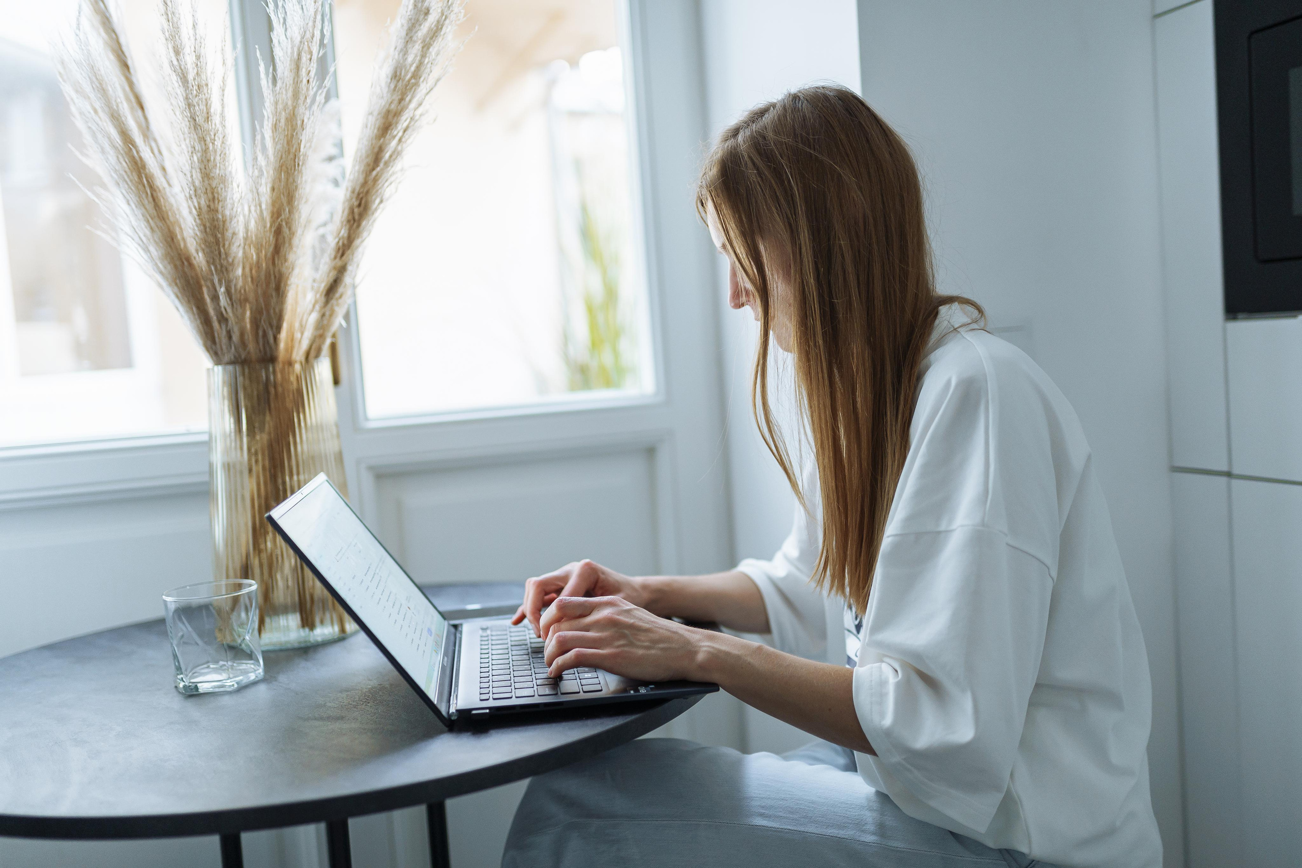 Робочий процес в офісі компанії - дівчина з відкритим ноутбуком сидить за столом біля вікна