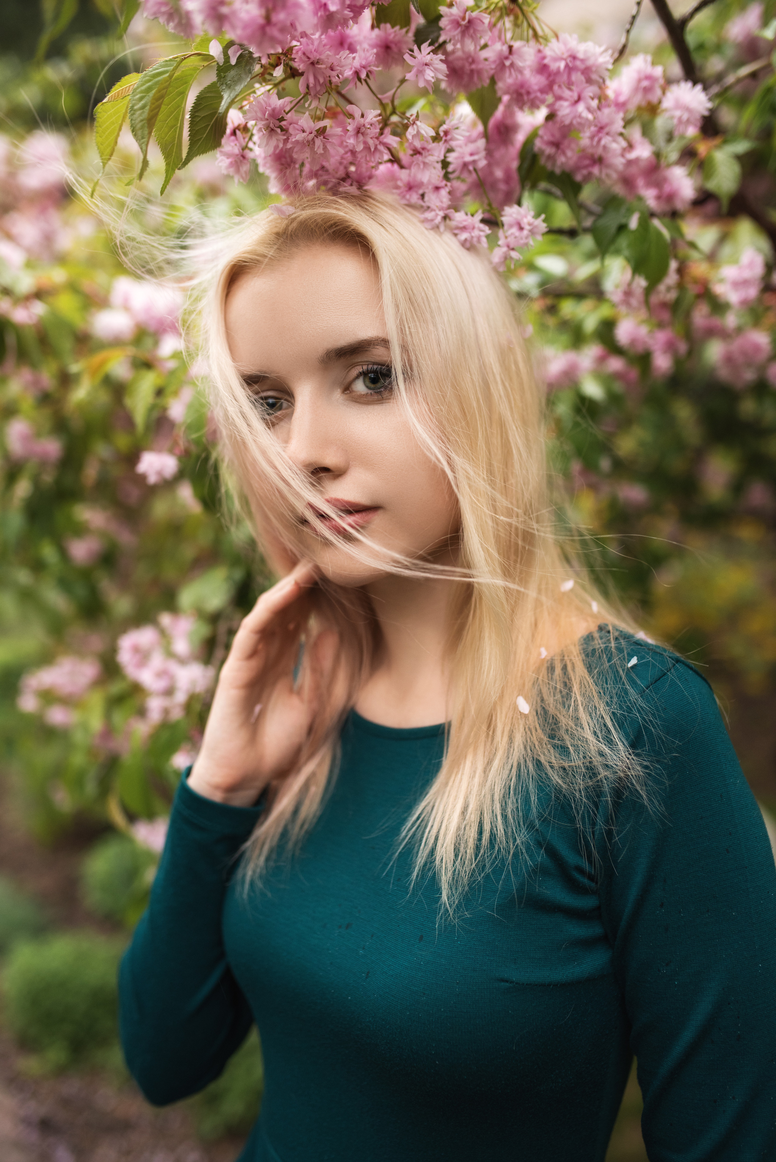 Весенний портрет девушки блондинки на фоне цветущей ветви в платье и рукой возле лица 