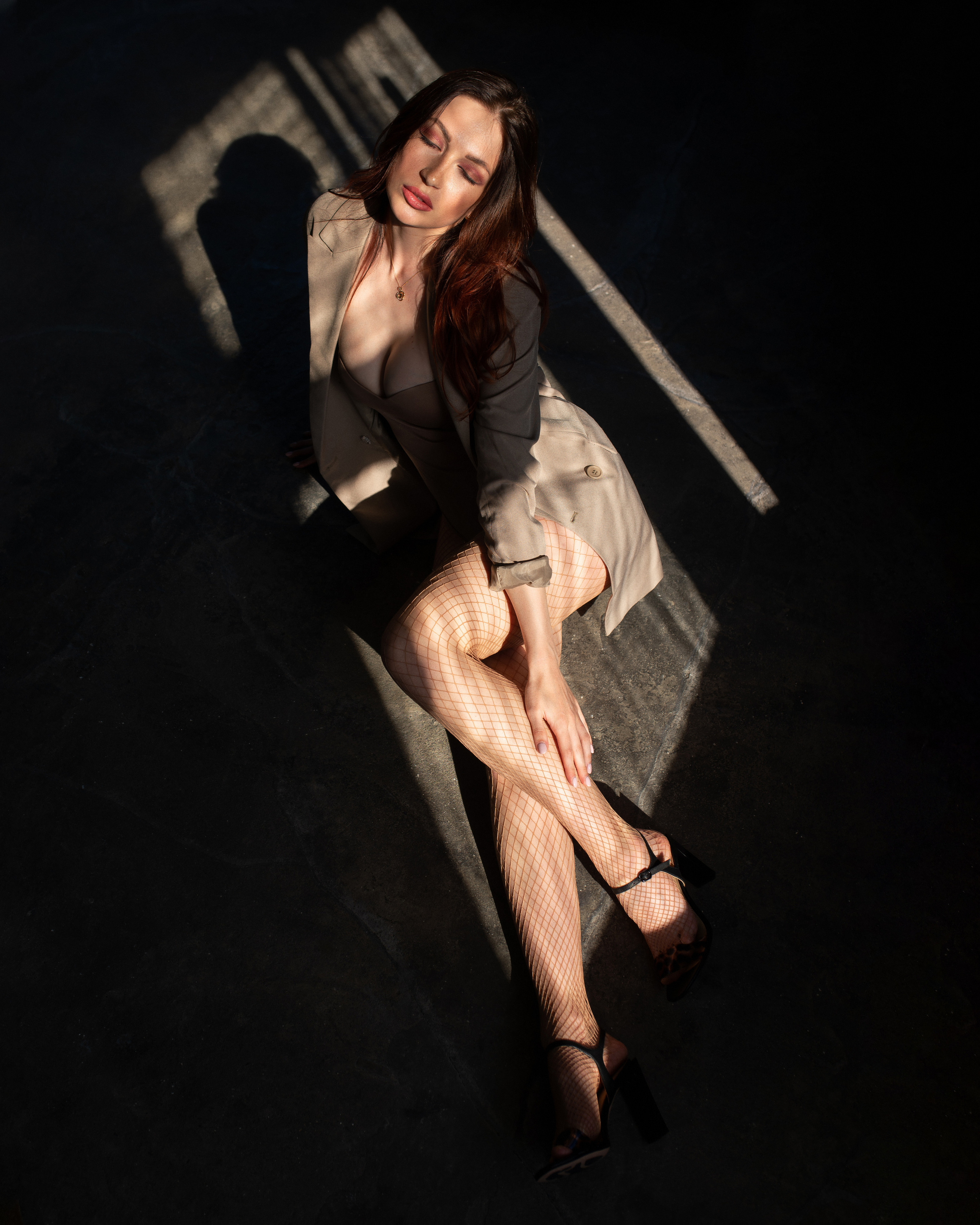 Ростовой  женский портрет. Девушка сидит на бетонном полу в студии, куда светит направленный луч солнечного света 