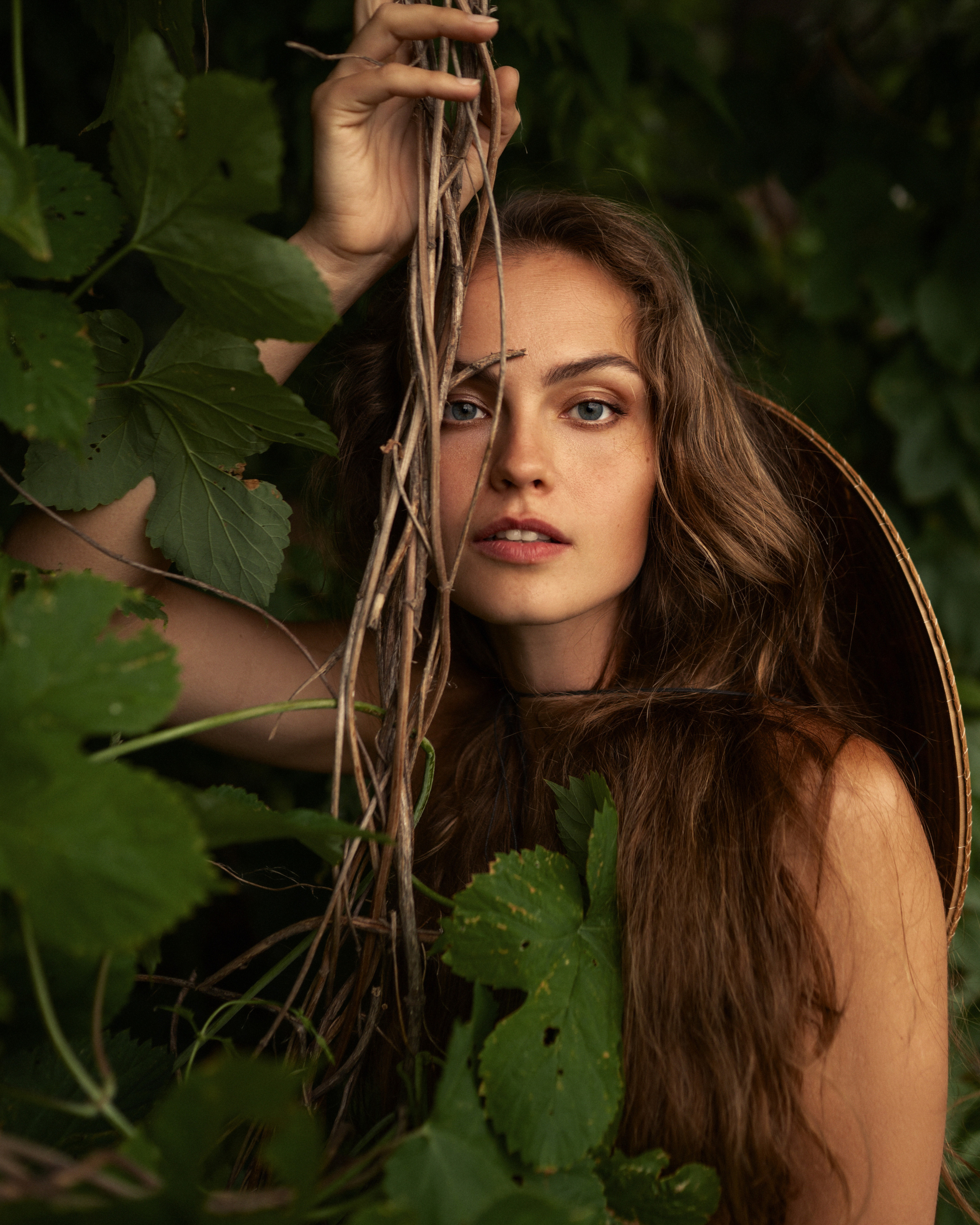 Крупный портрет девушки с густыми волосами  в зарослях леса с лианой на переднем плане 