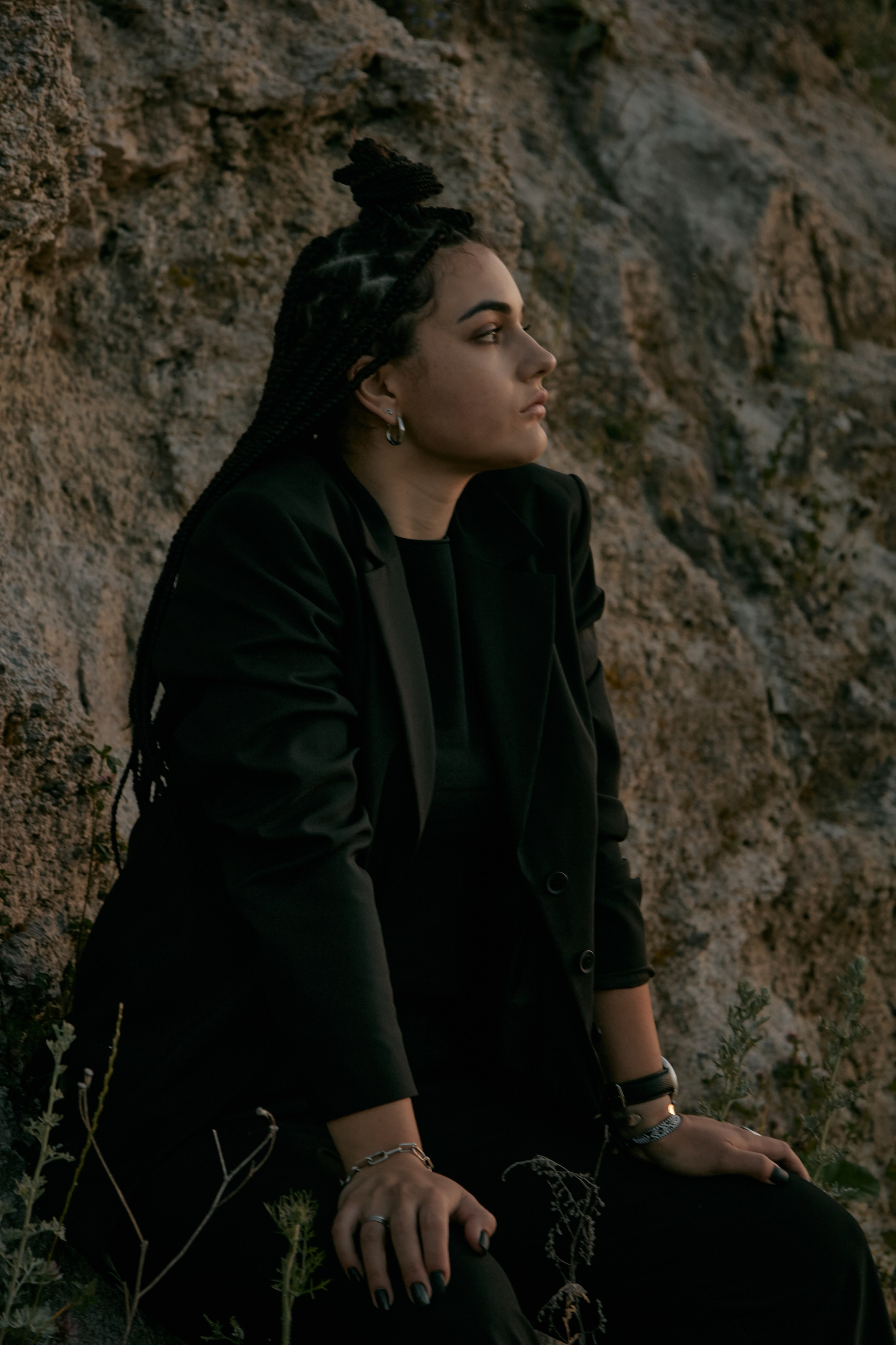 Молода жінка з афрокосами у чорному костюмі сидить на дерев'яному стільці у воді на тлі заходу сонця та зеленої природи