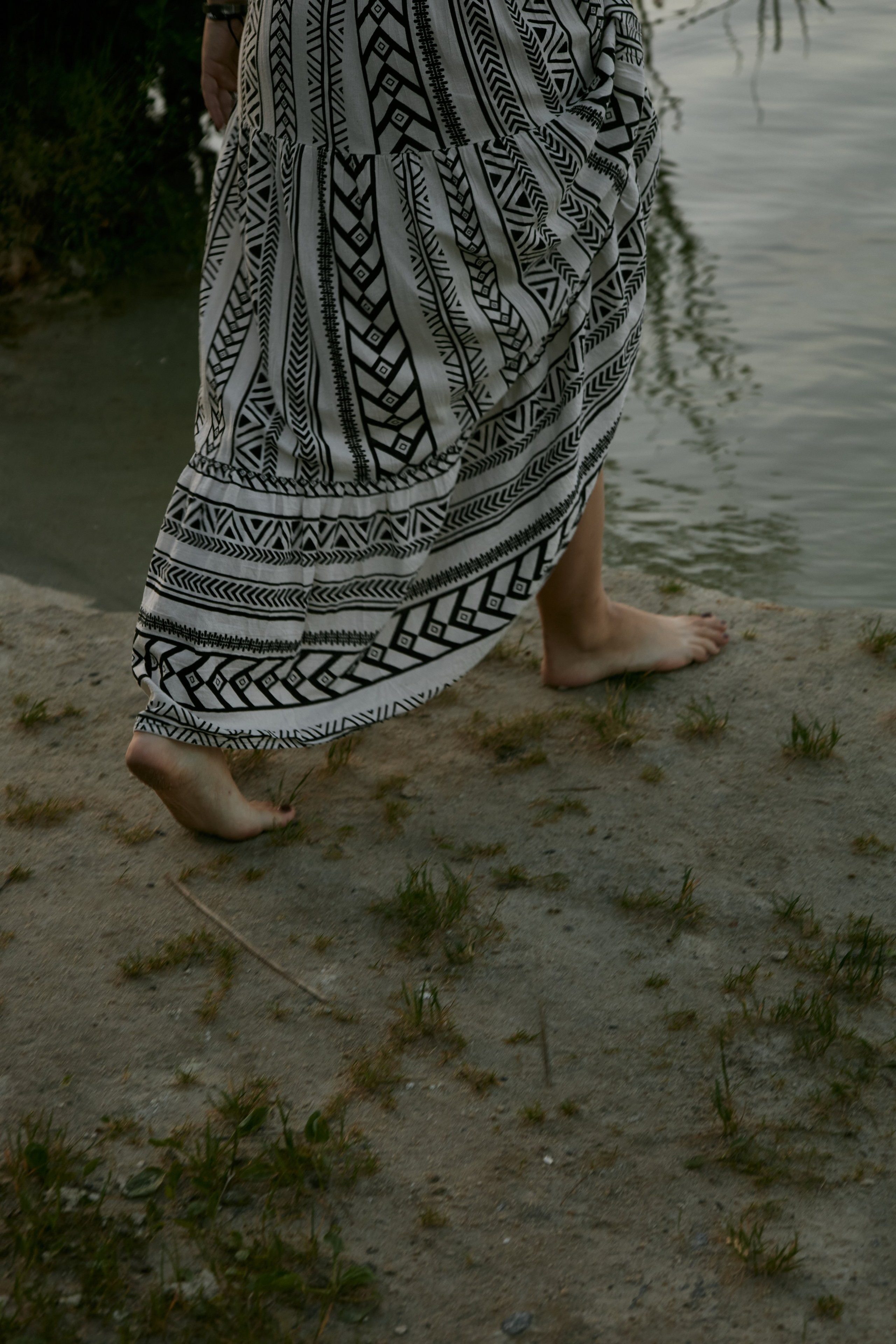 Молода жінка з афрокосами у чорному костюмі сидить на дерев'яному стільці у воді на тлі заходу сонця та зеленої природи