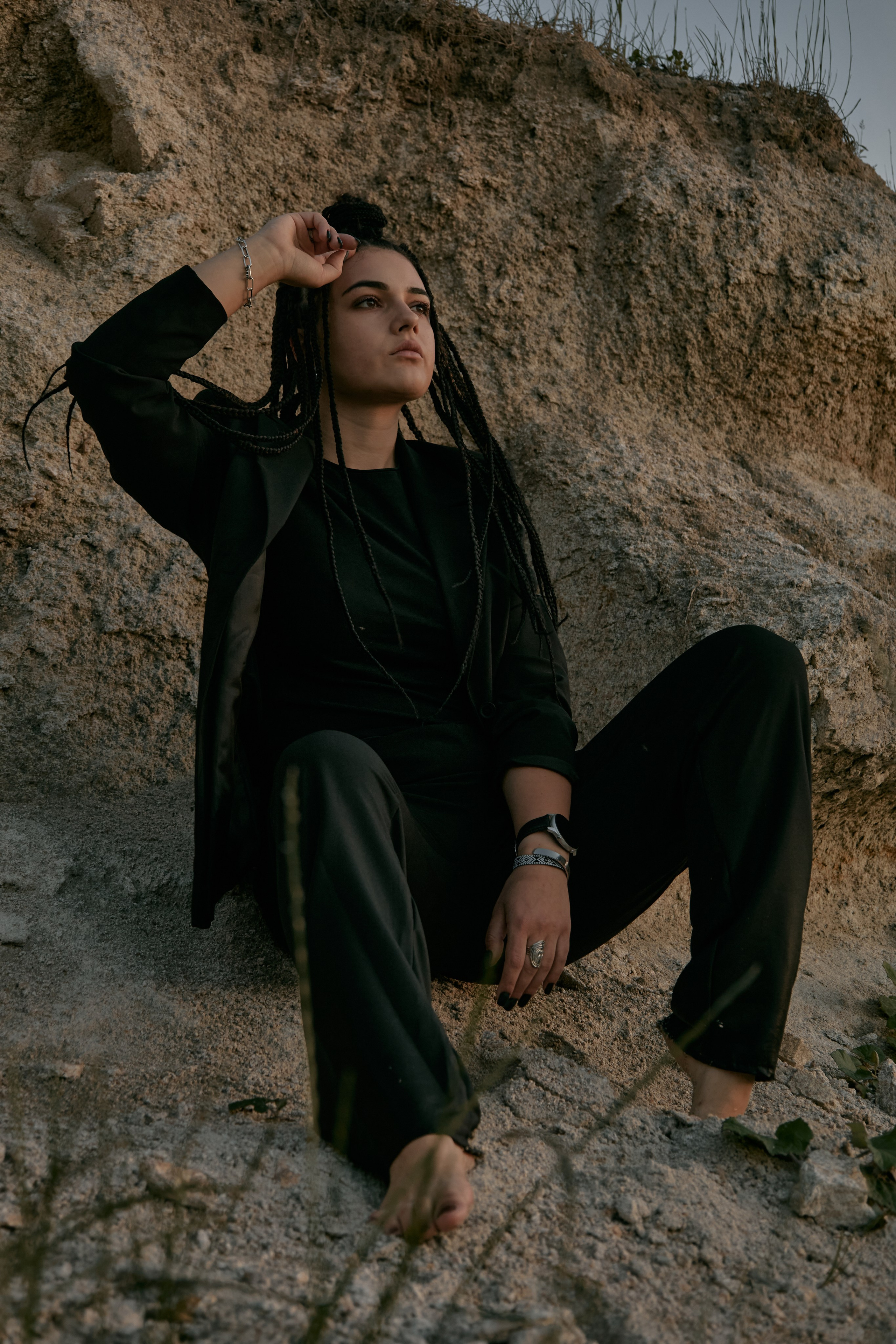 Молода жінка з афрокосами у чорному костюмі сидить на дерев'яному стільці у воді на тлі заходу сонця та зеленої природи