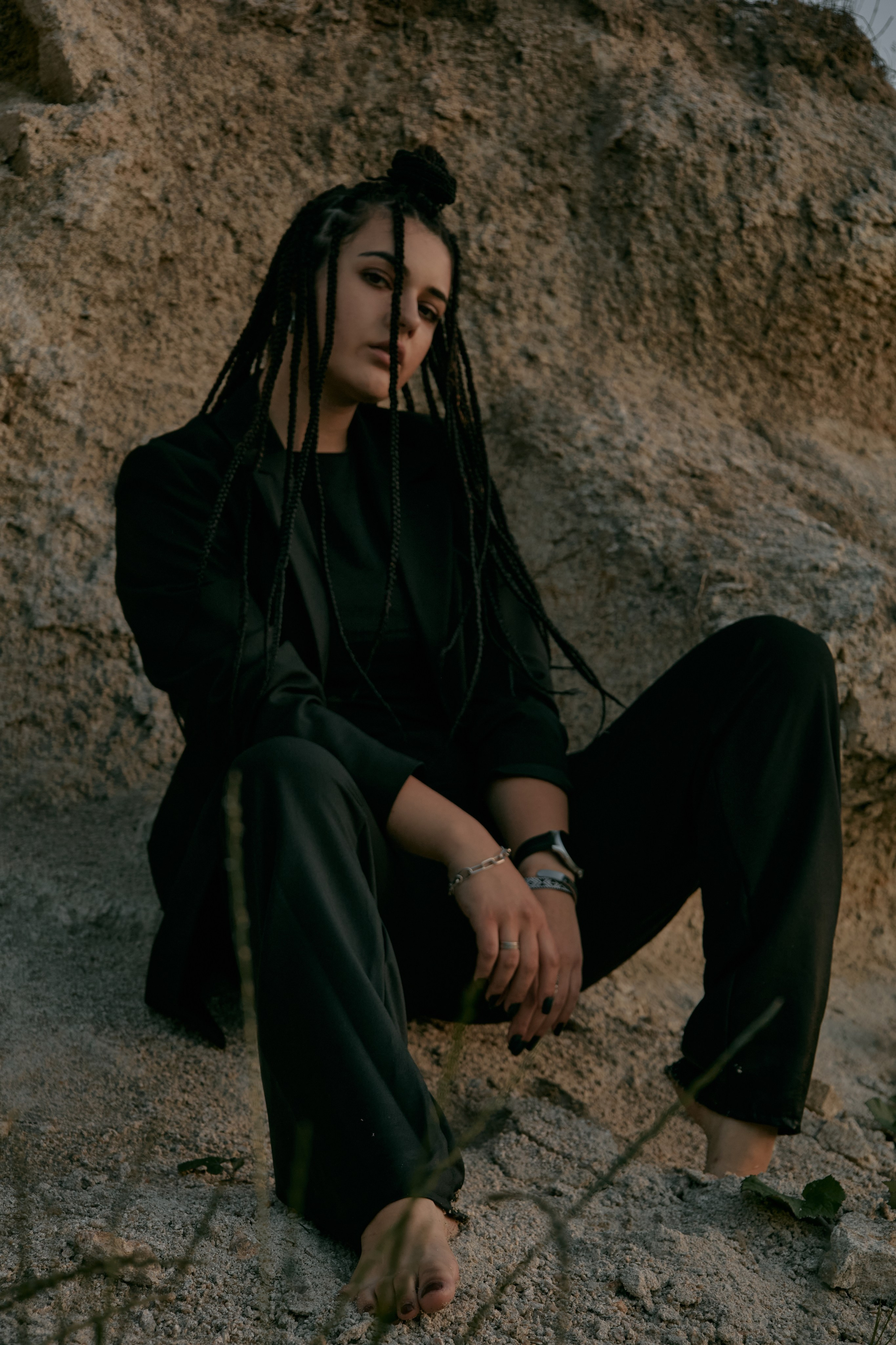 Молода жінка з афрокосами у чорному костюмі сидить на дерев'яному стільці у воді на тлі заходу сонця та зеленої природи