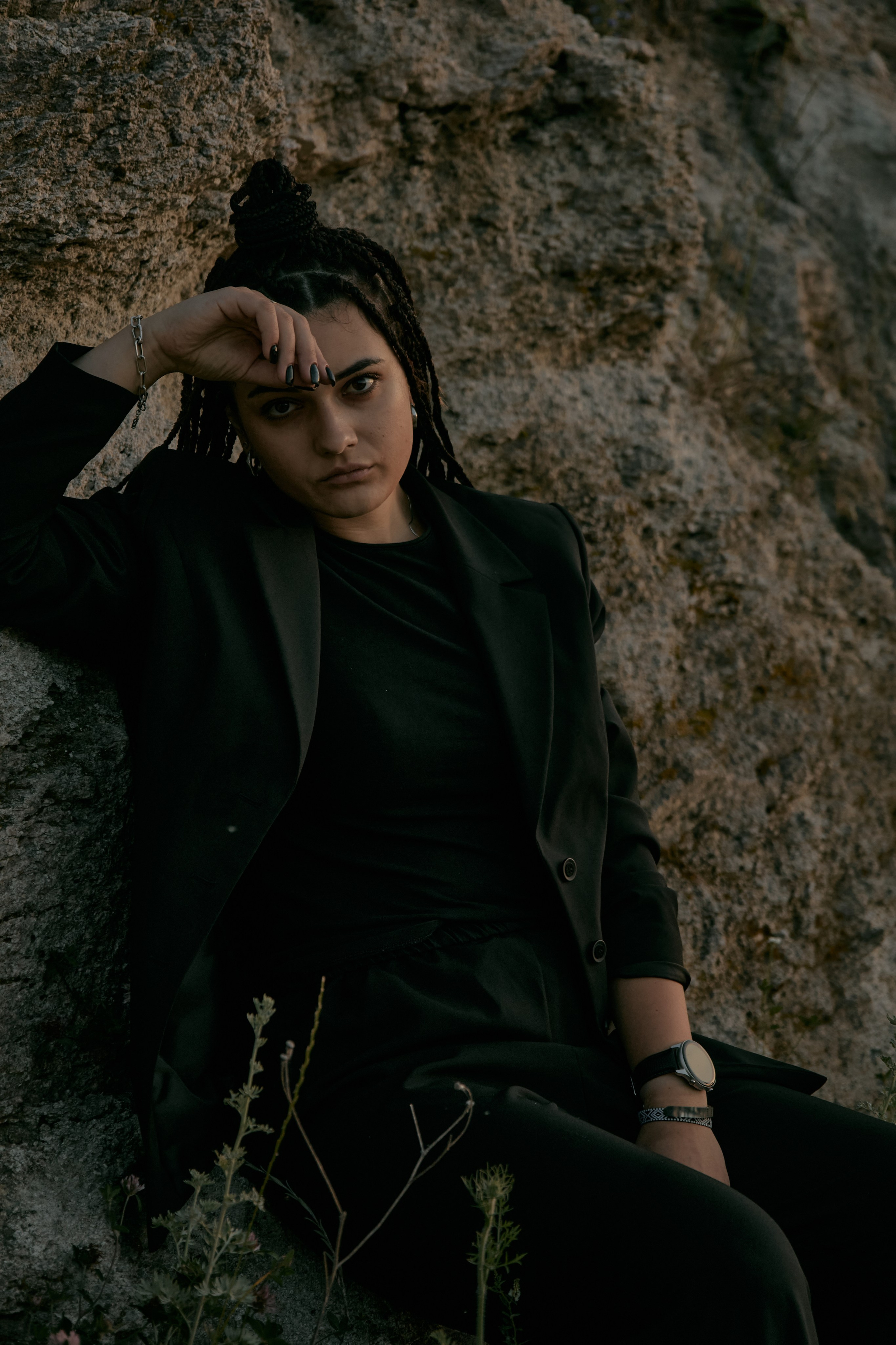 Молода жінка з афрокосами у чорному костюмі сидить на дерев'яному стільці у воді на тлі заходу сонця та зеленої природи