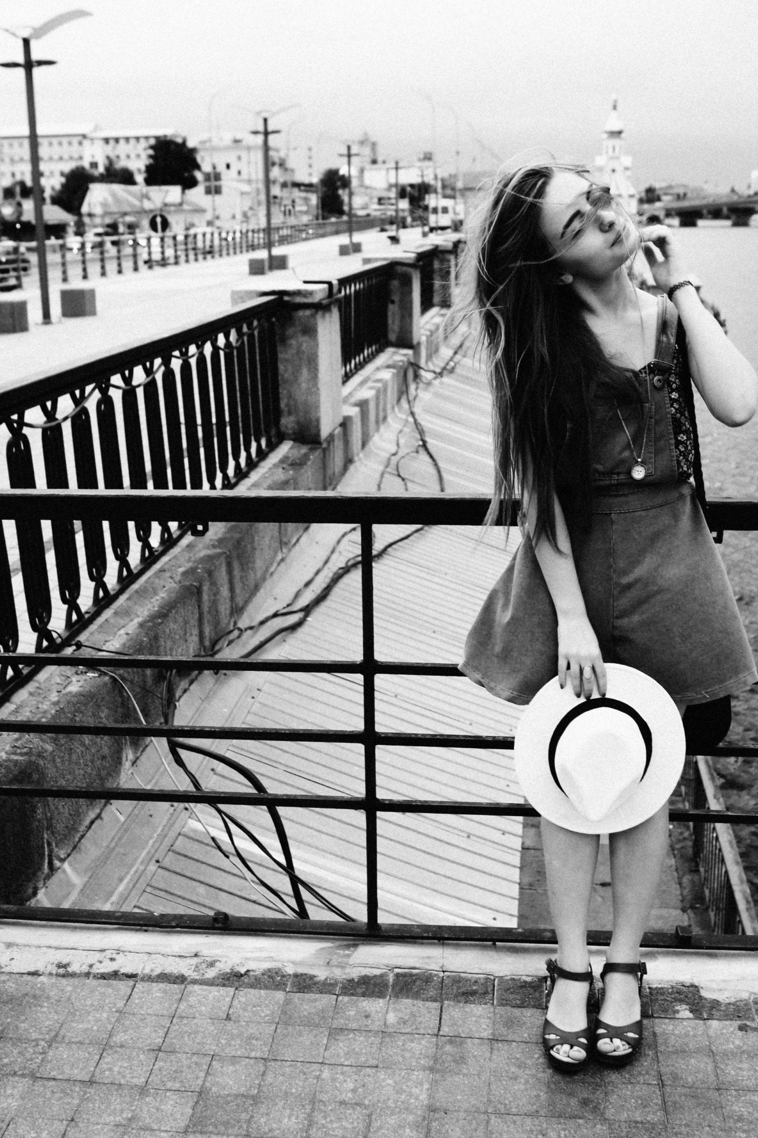 Девушка держит шляпу в руках и позирует на фоне речки и моста