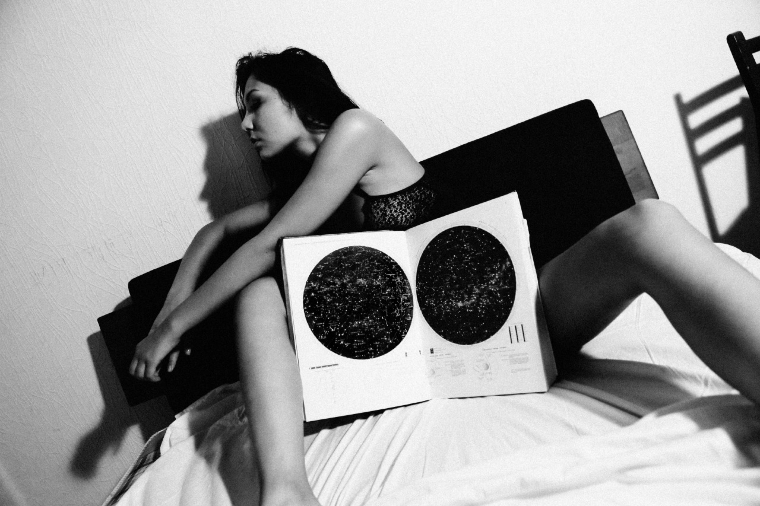 Девушка в купальнике сидит на кровати, между ног открытая книга