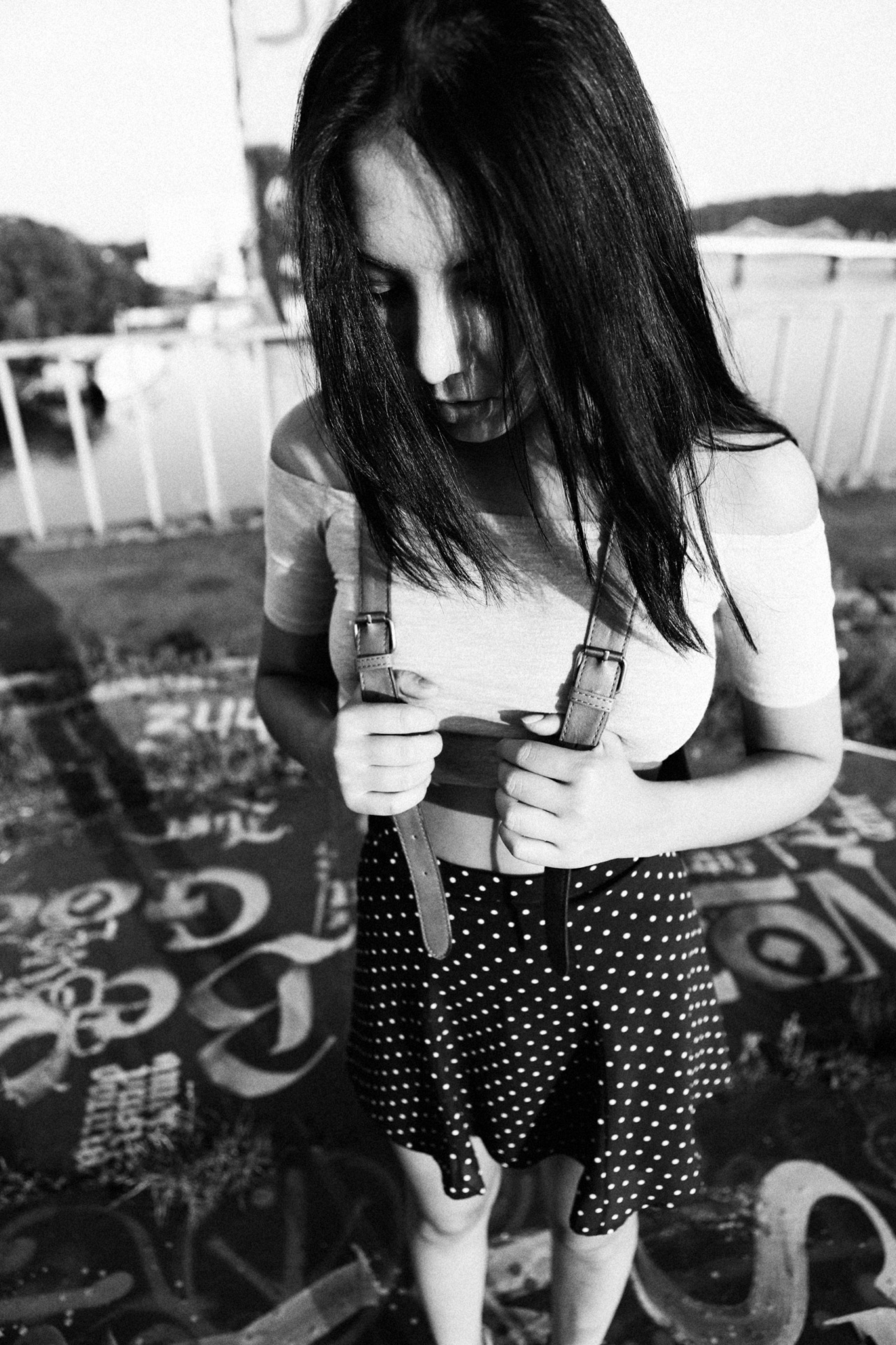 Девушка азиатской внешности стоит на мосту, прикрыв лицо волосами, и держит шлейки рюкзака в руках