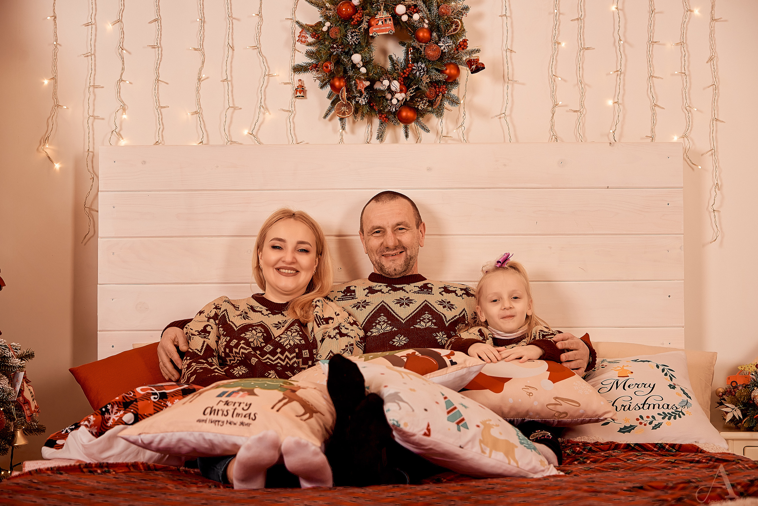 Рождественское фото на кровати, мама папа и дочь в подушках.