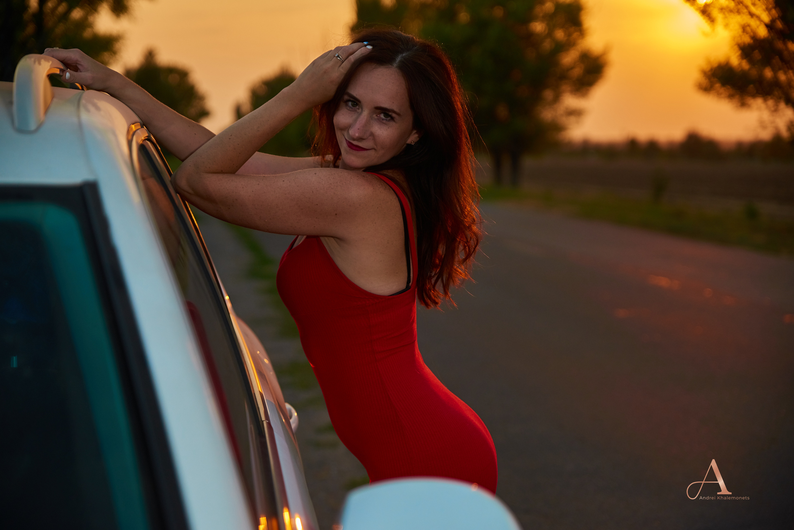 Девушка позирует в красном платье у автомобиля.