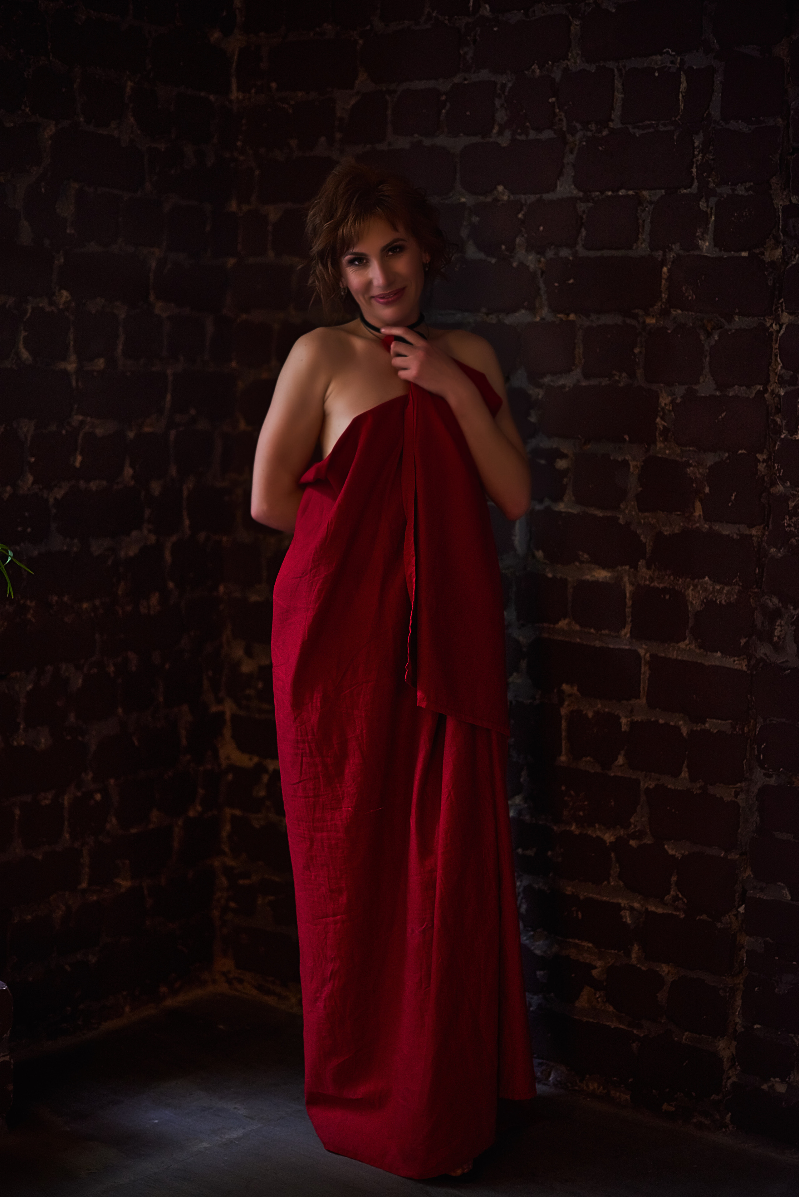 Девушка укуталась в красную простынь, подготовка к ню фотосессии.