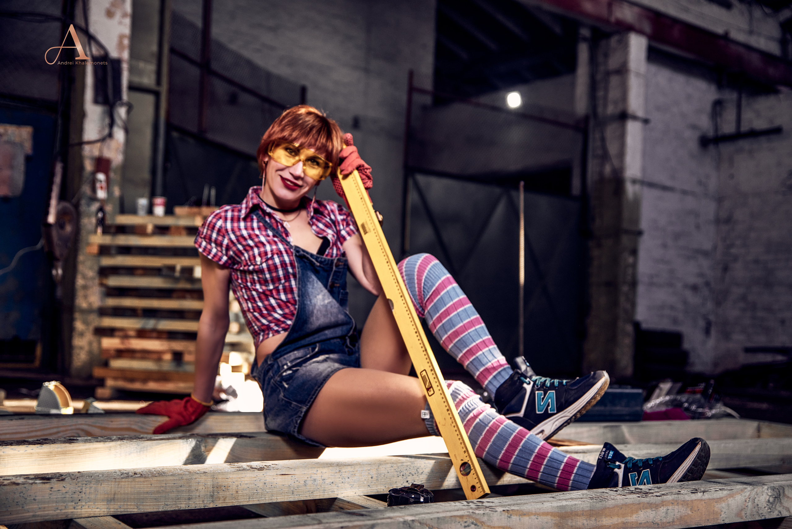 Рыжеволосая девушка позирует со строительным уровнем в слесарной мастерской.