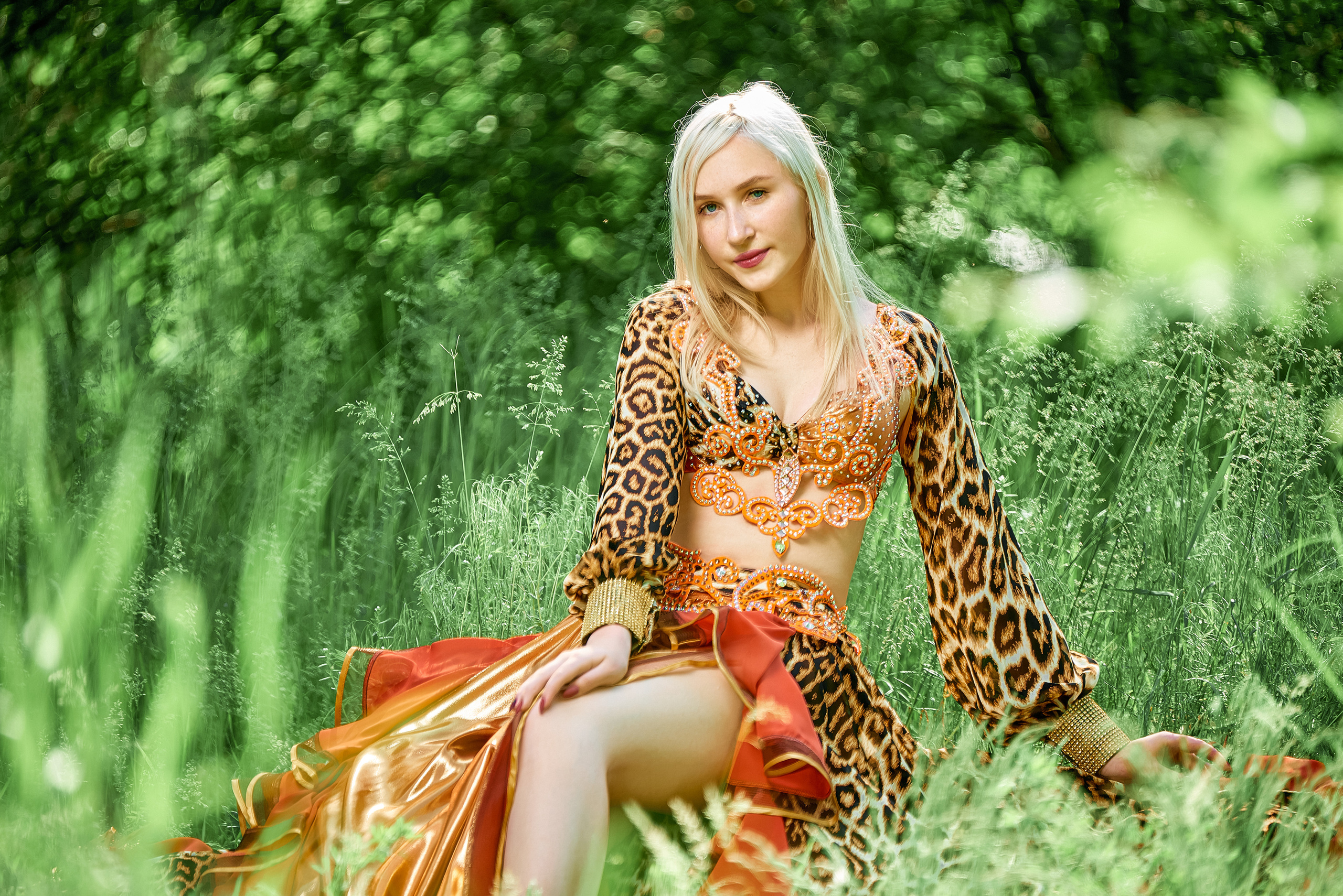 Беловолосая девушка в красном бальном платье, отдыхает на лесном лугу.