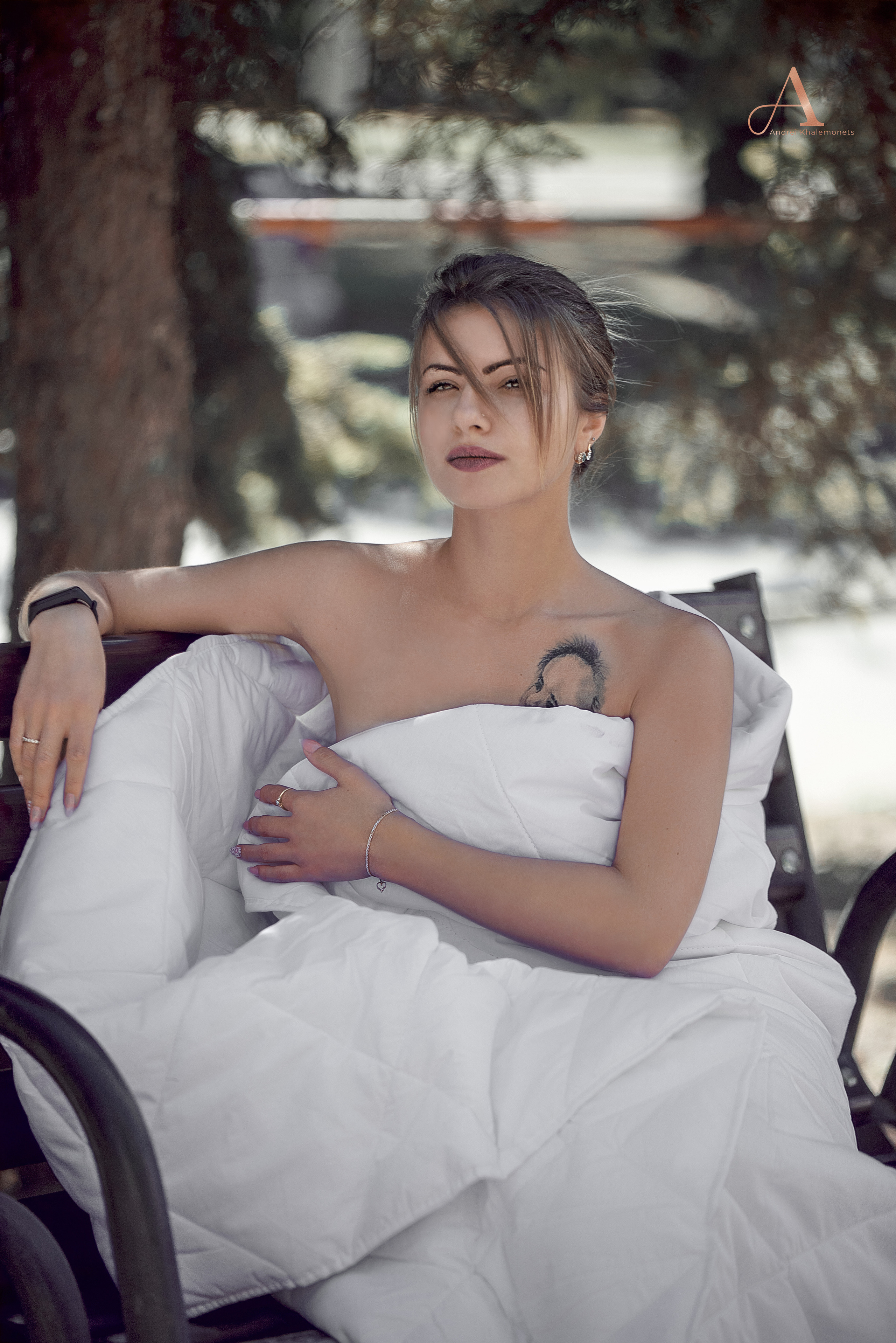 Обнаженная девушка в одеяле на скамье в общественном месте.