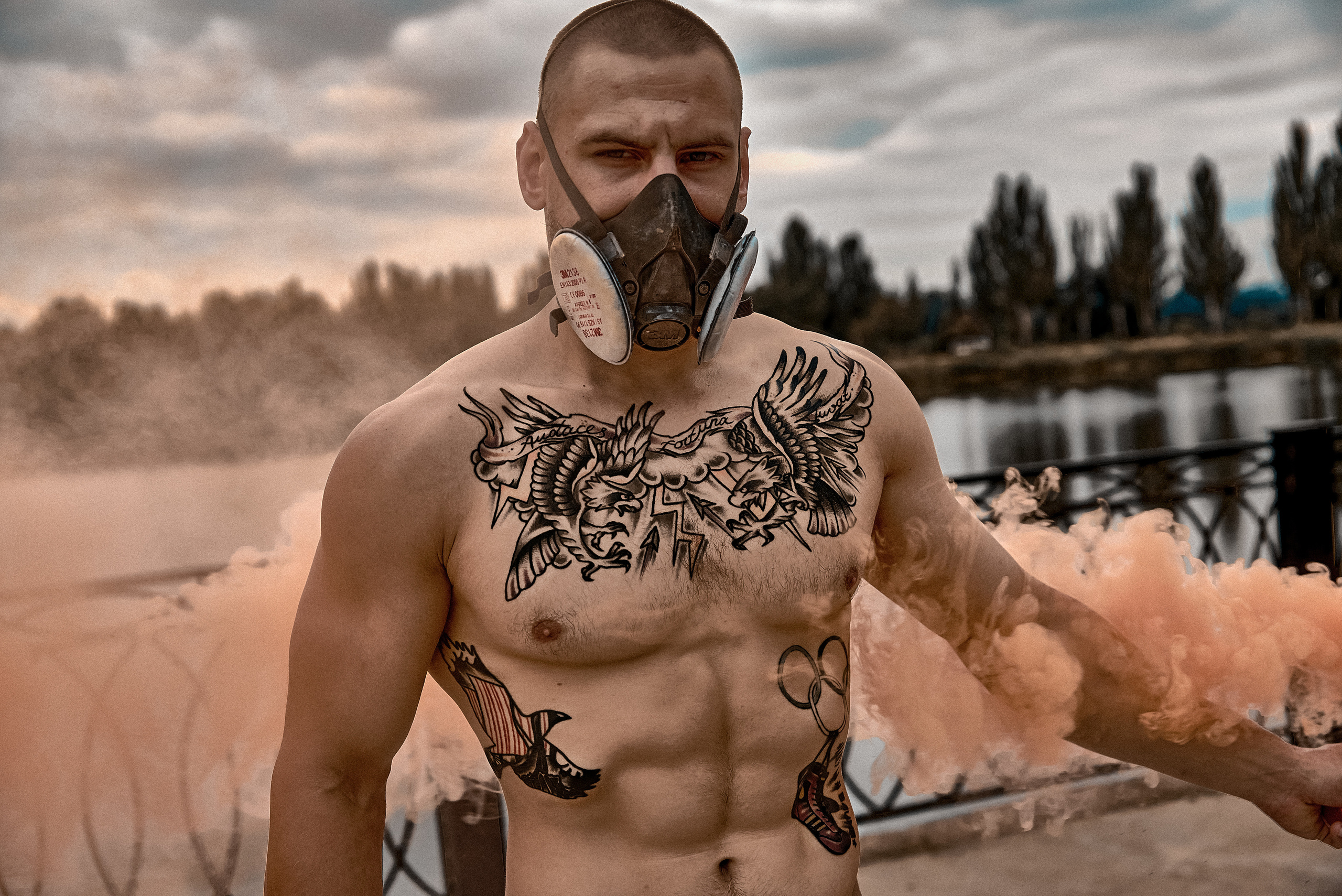 Накачаный парень с множеством тату, фотосессия с цветным дымом.