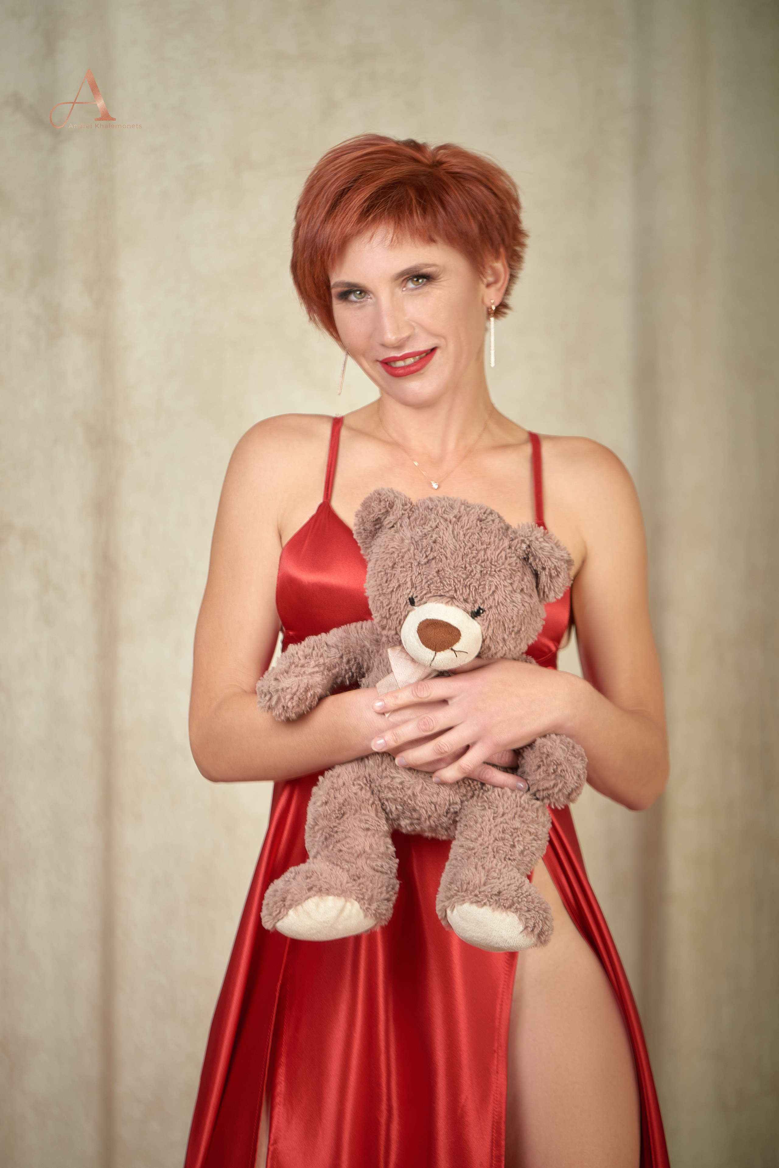 Девушка в красном платье с плюшевым мишкой в руках.
