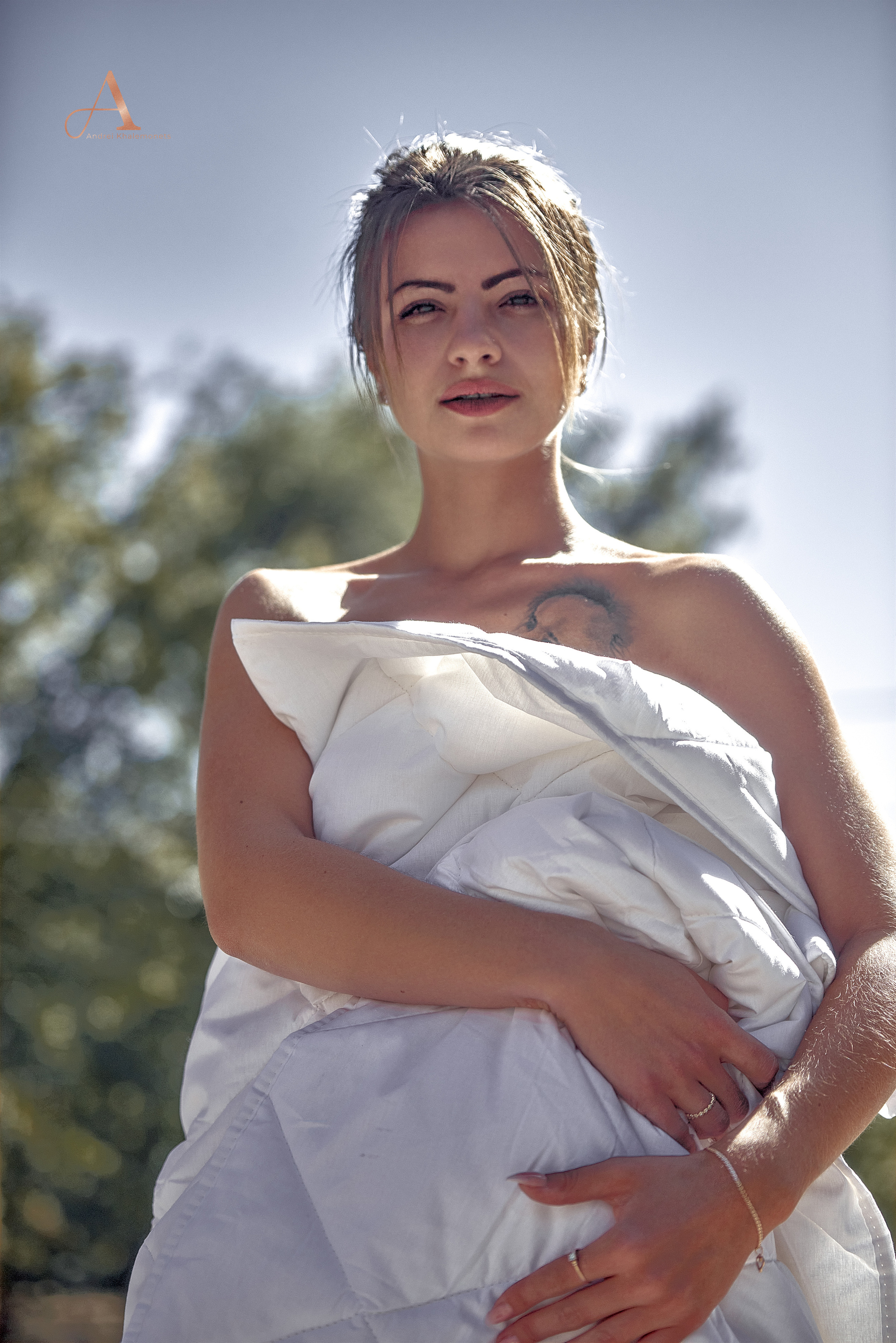 Девушка с тату на плече позирует в одеяле.