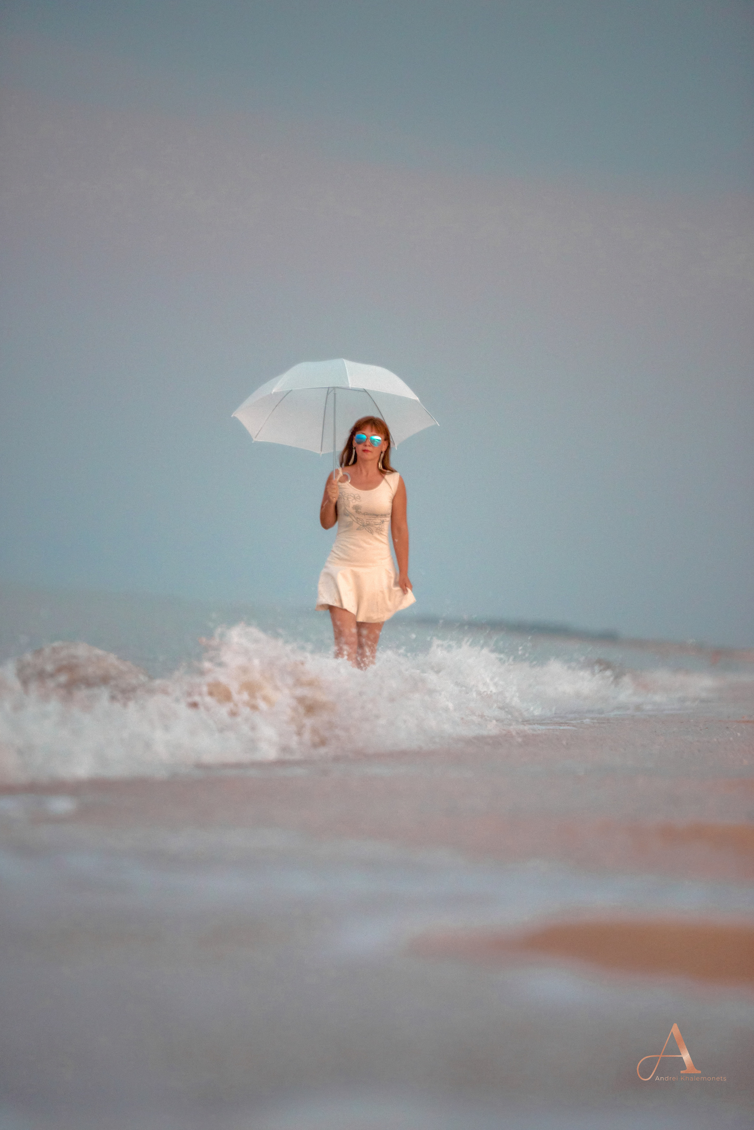 Девушка в платье среди морских волн с зонтиком.