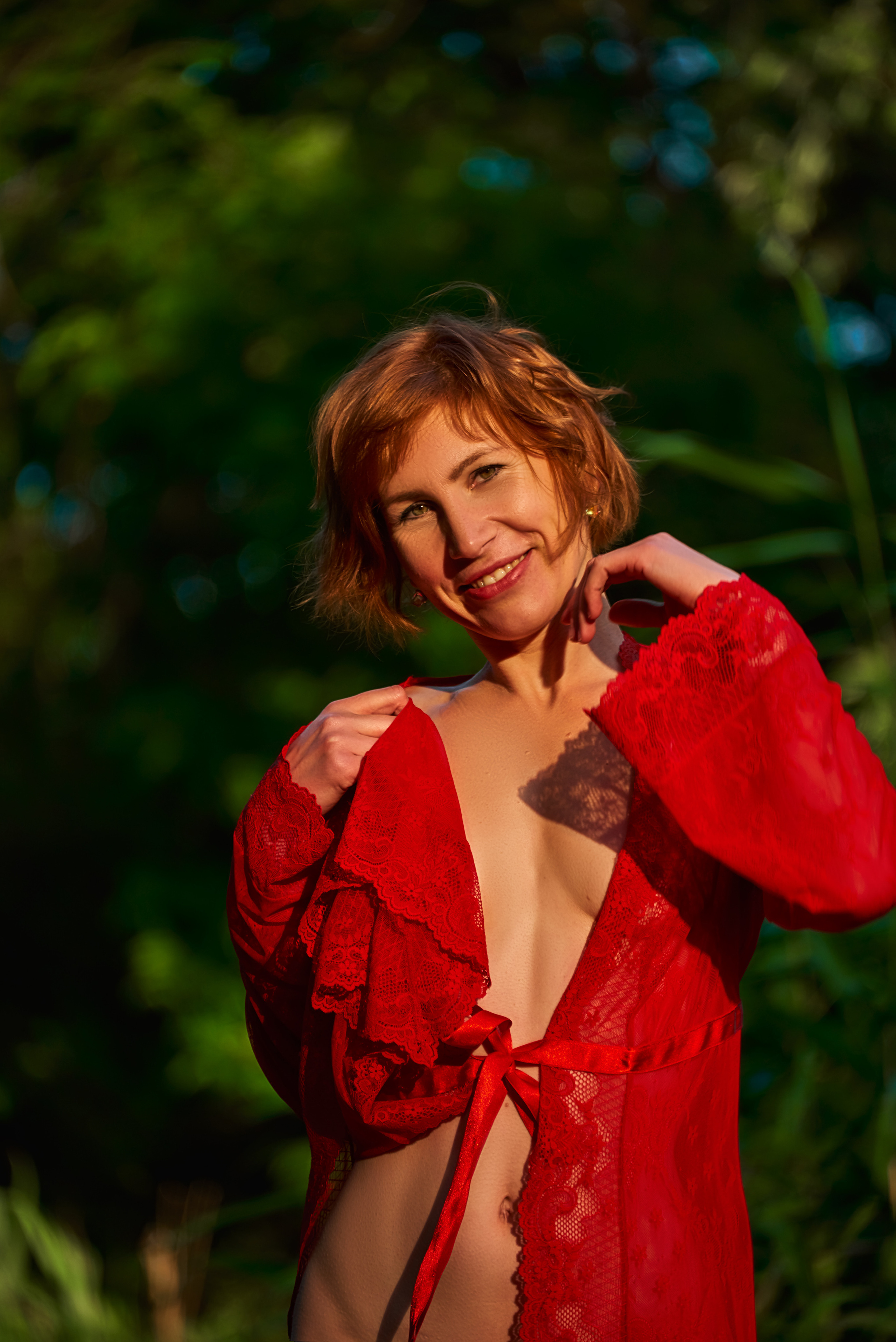 Девушка позирует ню на природе в красном пеньюаре.