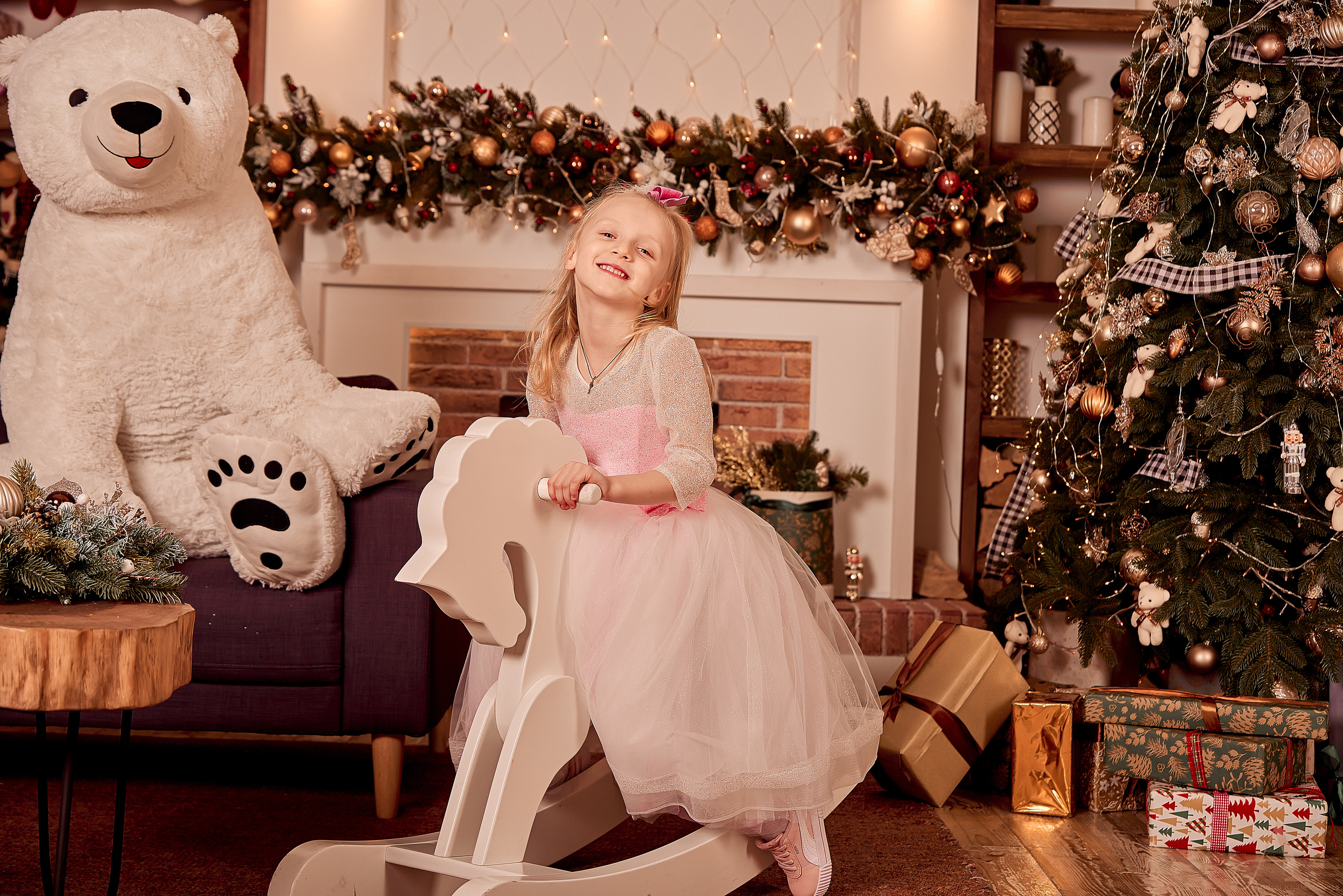 Девочка в розовом платье катается на игрушечной лошади.