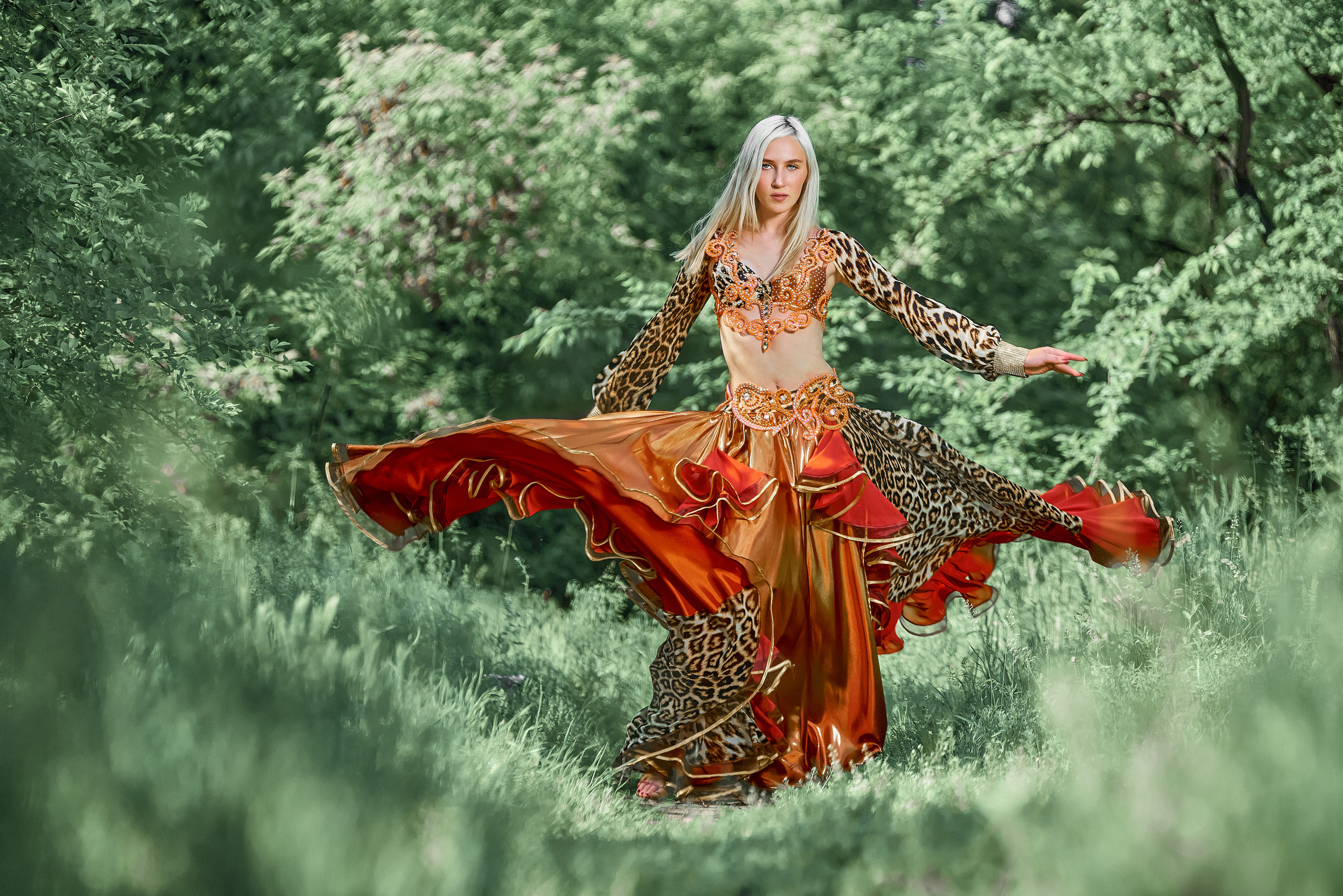 Девушка танцует в красном бальном платье на лесной тропинке.