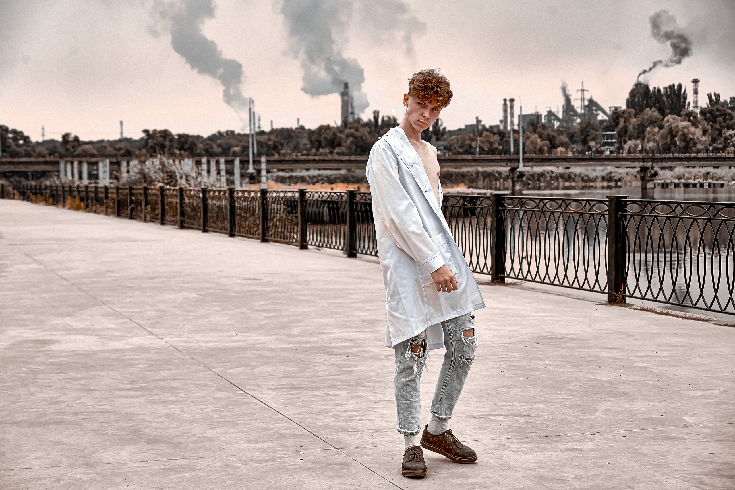 Парень в белом халате на фоне выбросов дыма промышленным заводом.