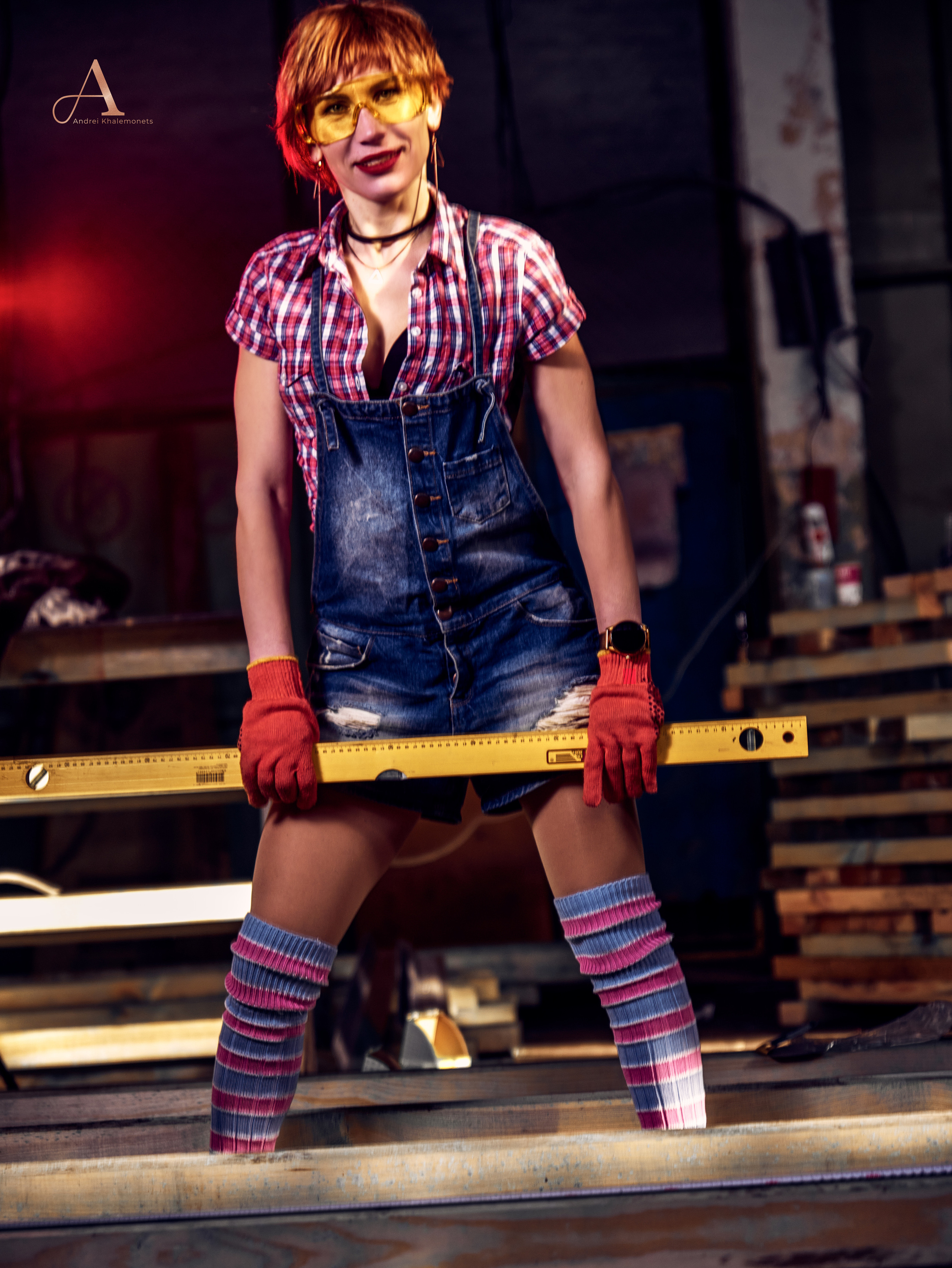 Девушка в джинсовом комбинезоне и строительном уровнем в руках.