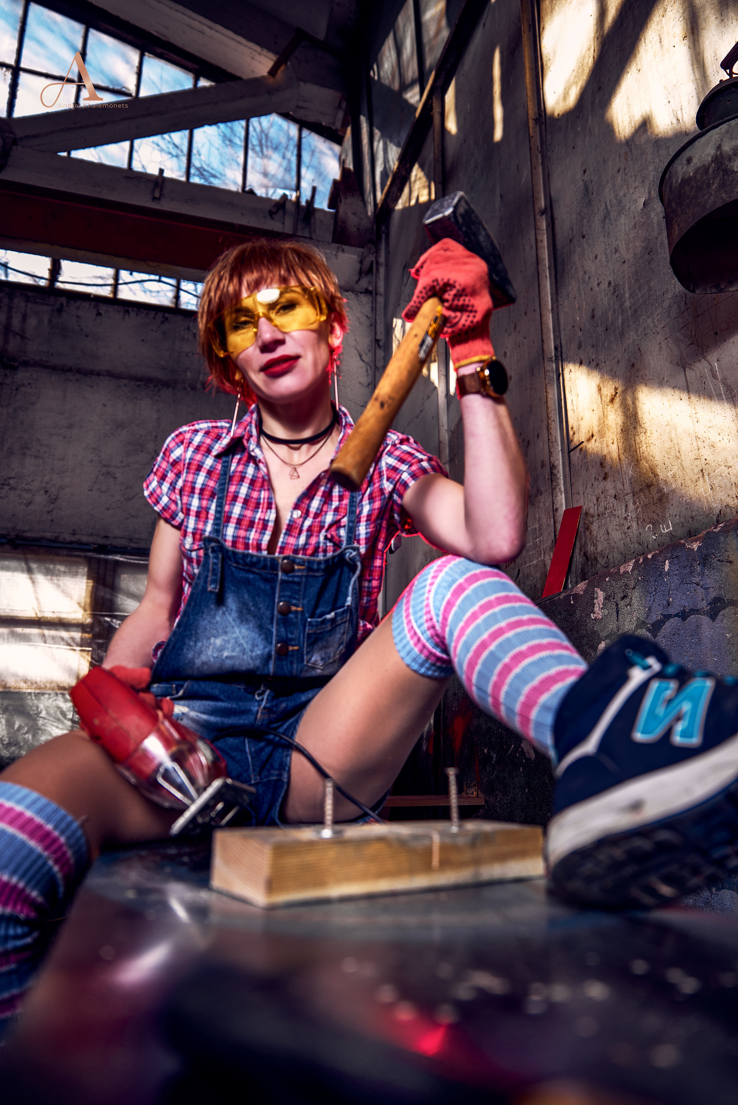 Девушка в защитных очках с молотком и электролобзиком в руках.