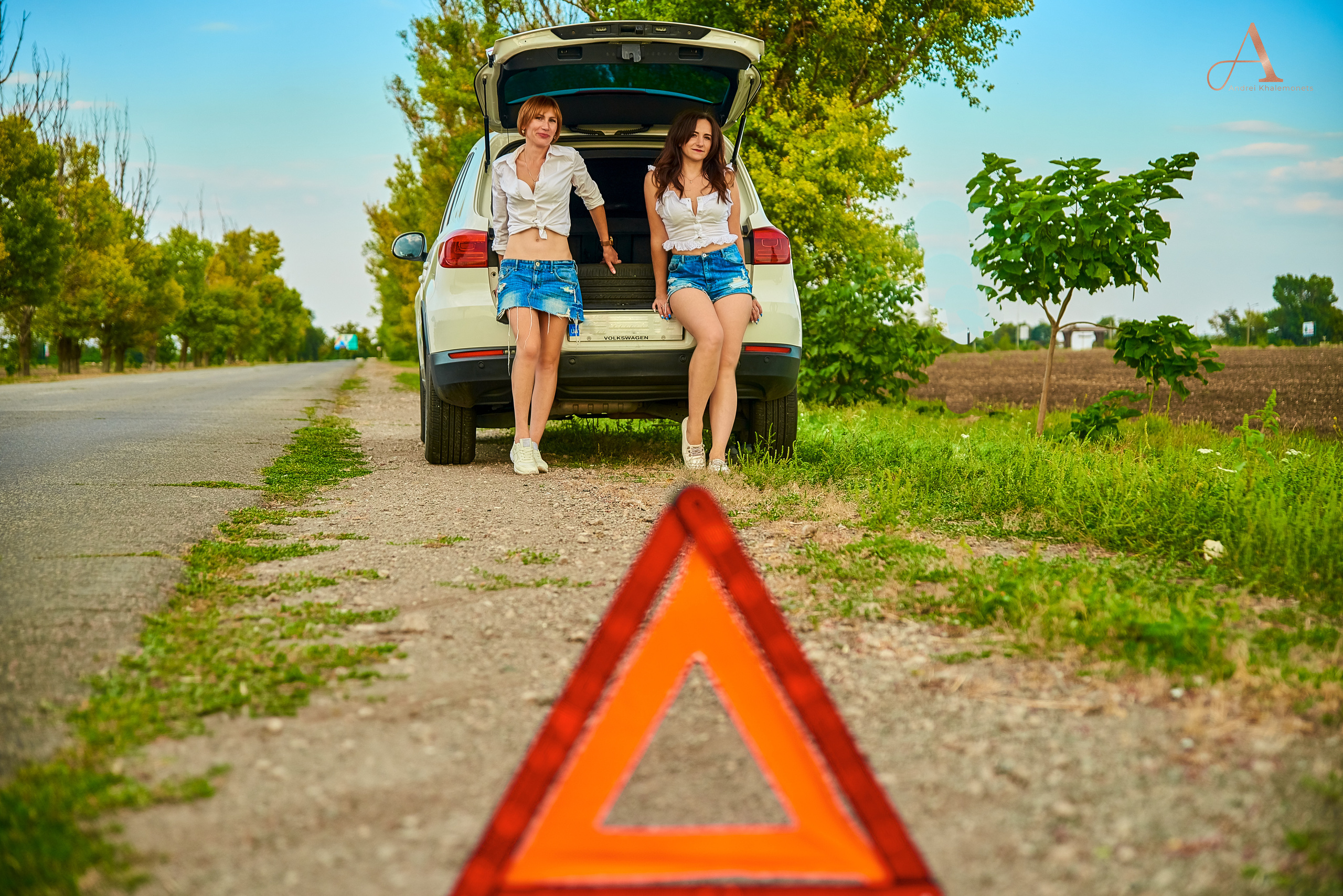 Знак аварийной ситуации на дороге и две девушки в багажнике автомобиля.